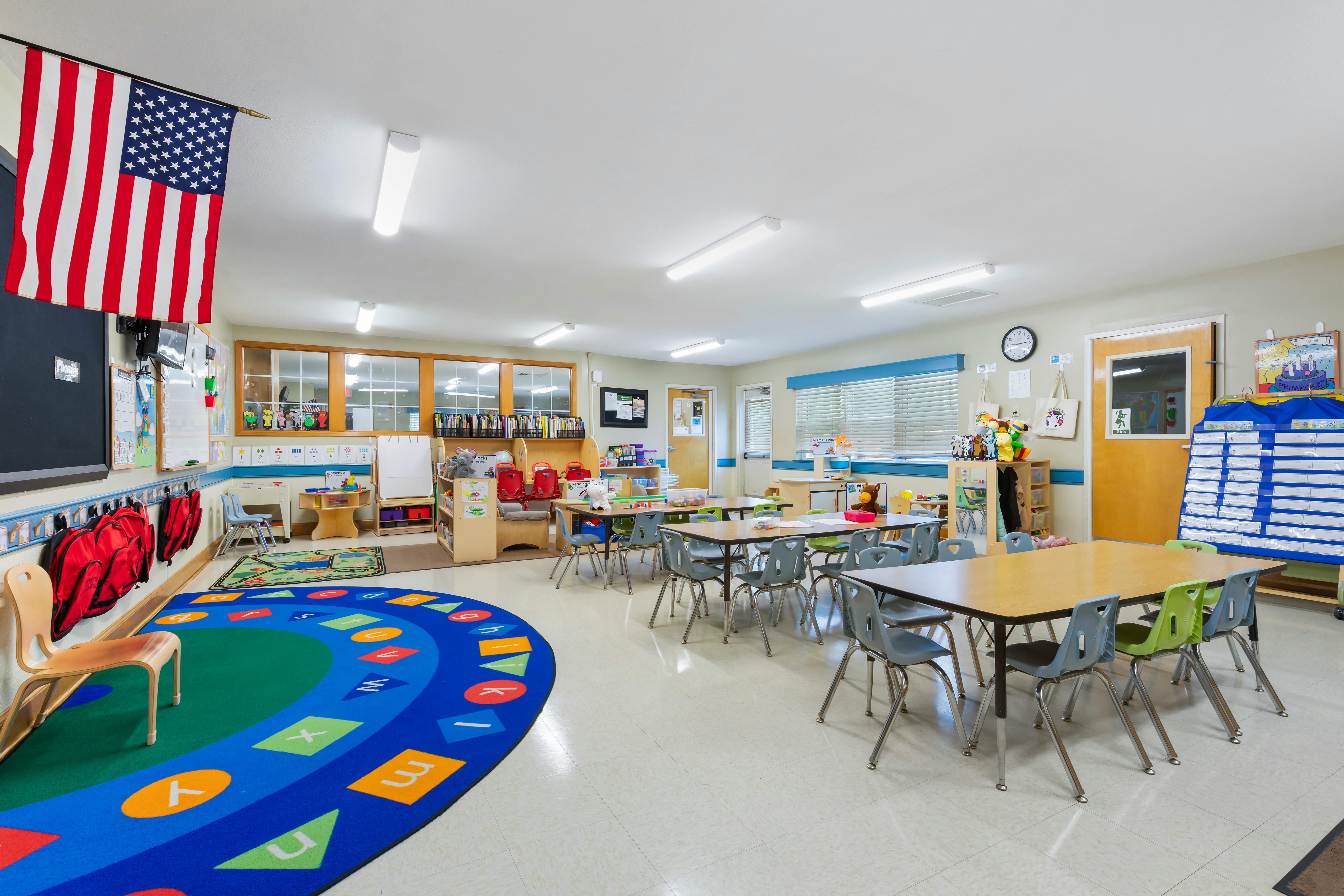 An empty classroom with small tables, chairs, and an alphabet rug