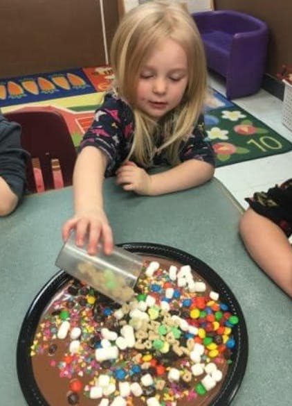 Child pouring toppings onto a dessert in a classroom