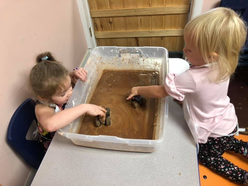 Two children playing with toys in a bin of muddy water