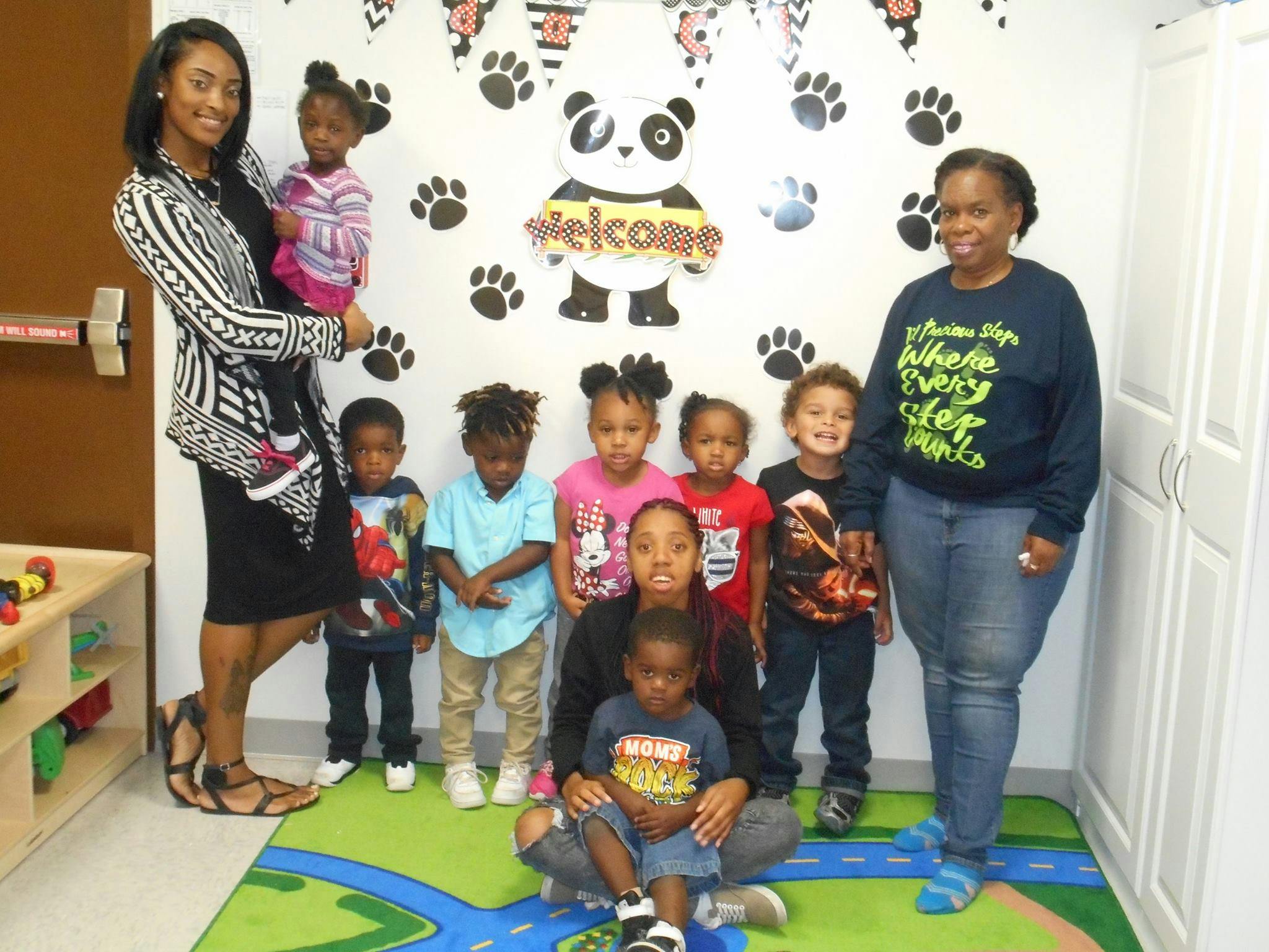 Two people with a group of children in a room with a panda decoration