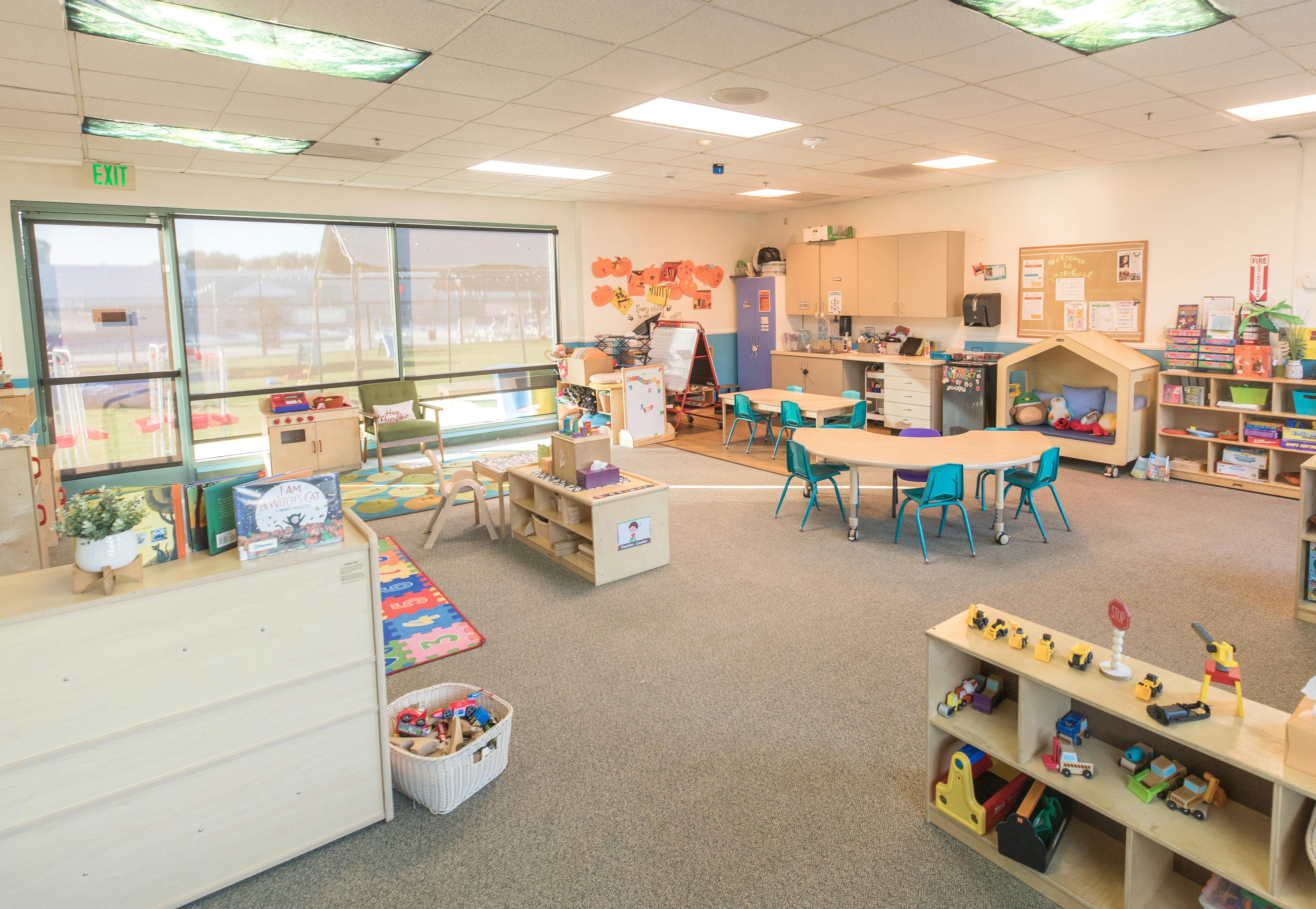 Empty classroom with small tables and chairs, toys, and shelves