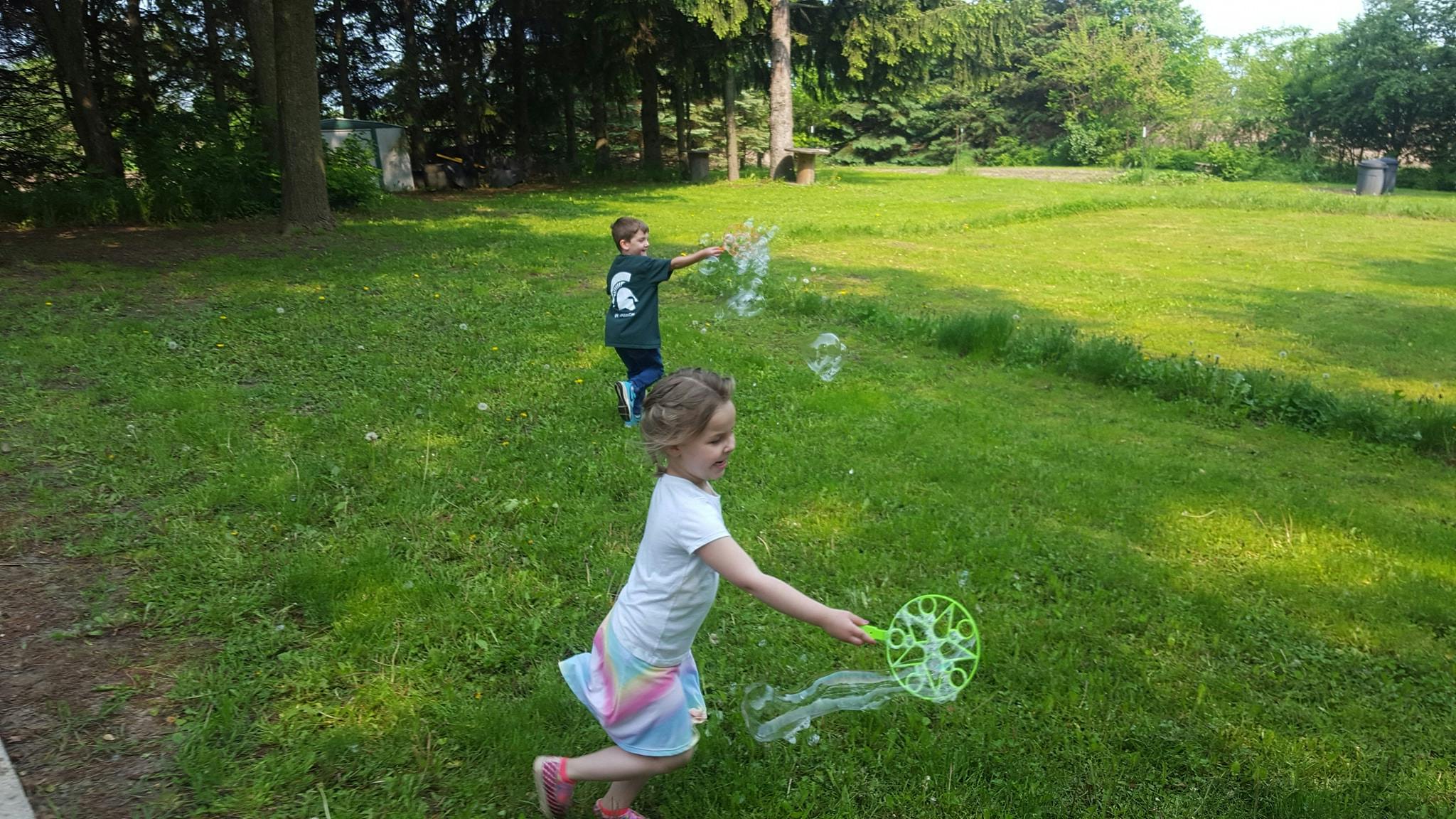 Two children blowing bubbles in a grassy field