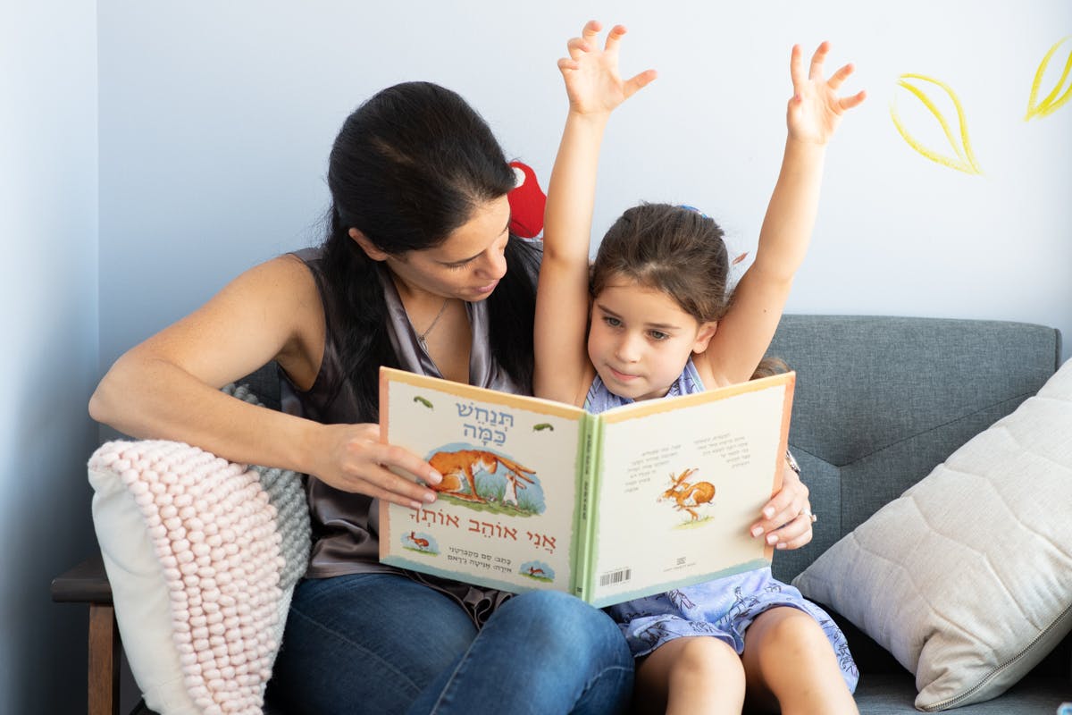 Person and child reading a book, child has arms raised
