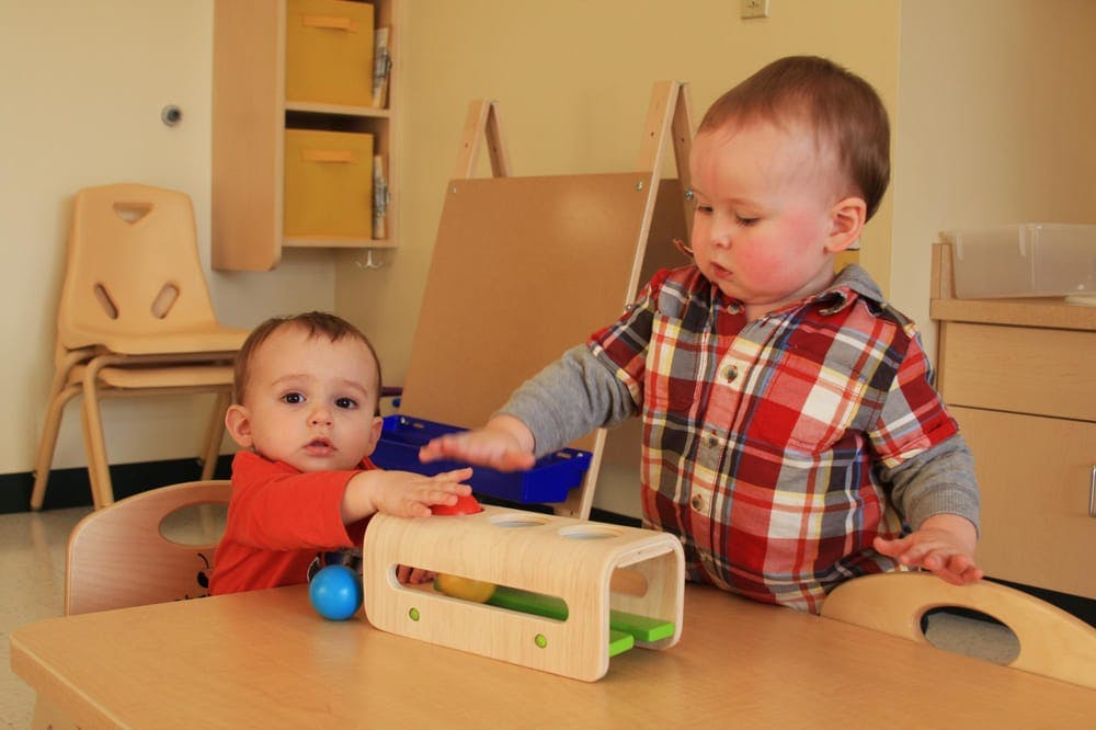 Two children playing with a toy on a table in a classroom