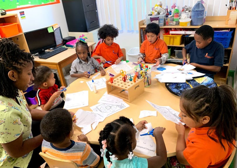 Adult and children gathered around a table doing an activity in a classroom