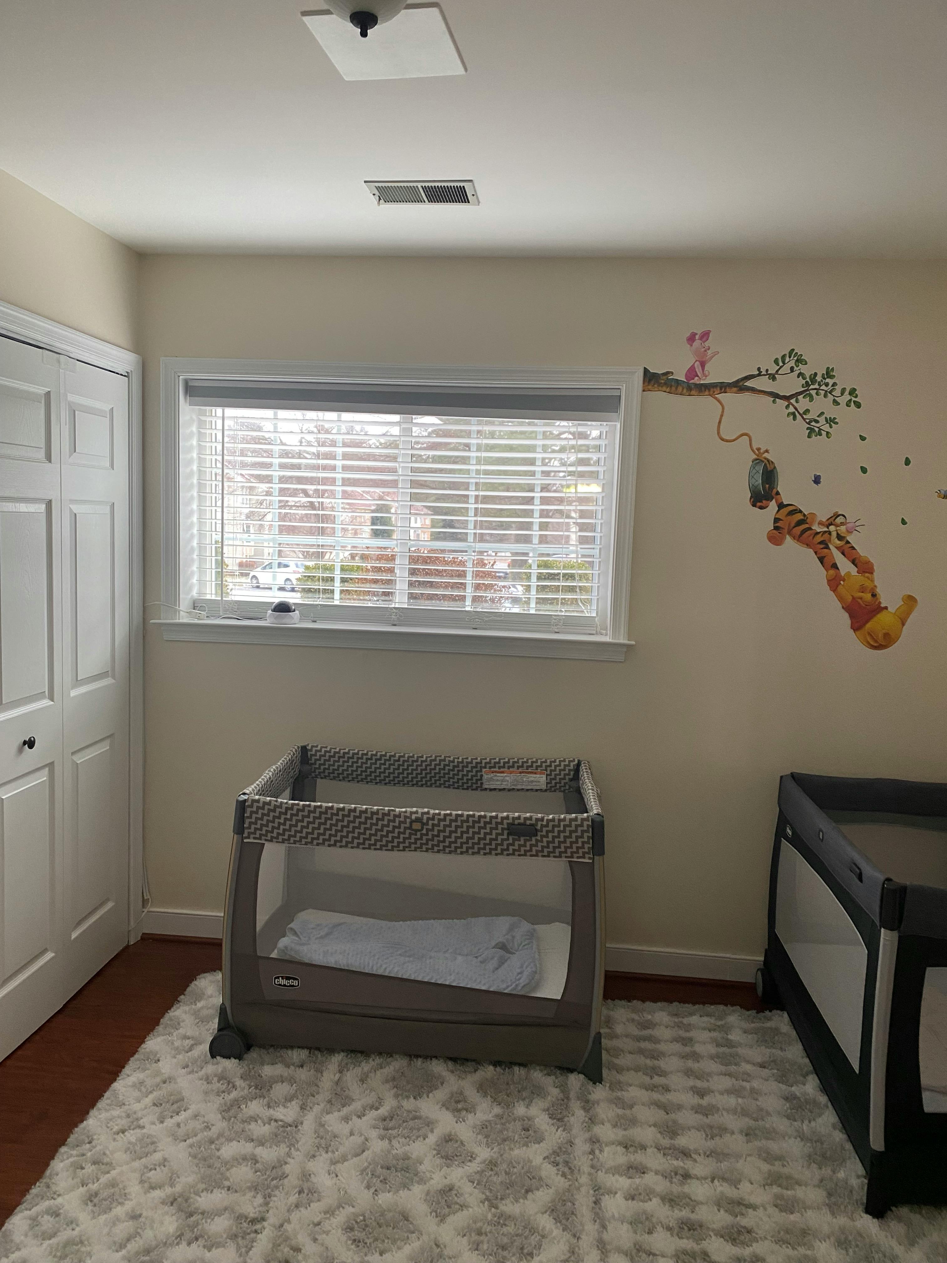 Two empty baby cribs in a room with a window and wall decals