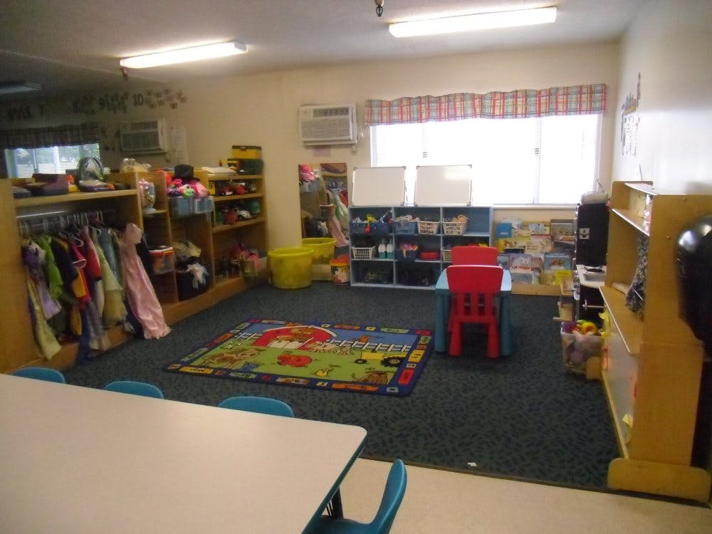 Empty classroom with small tables, chairs, and shelves with toys and books on shelves