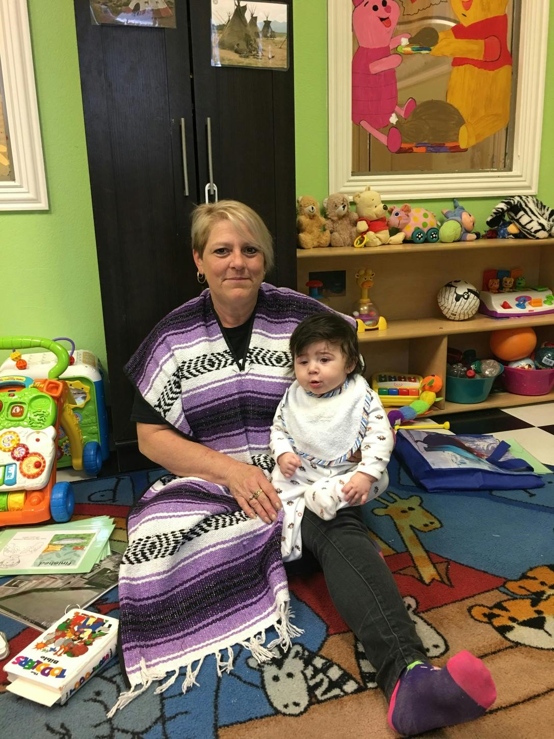 Person sitting on floor holding a child in a room with toys