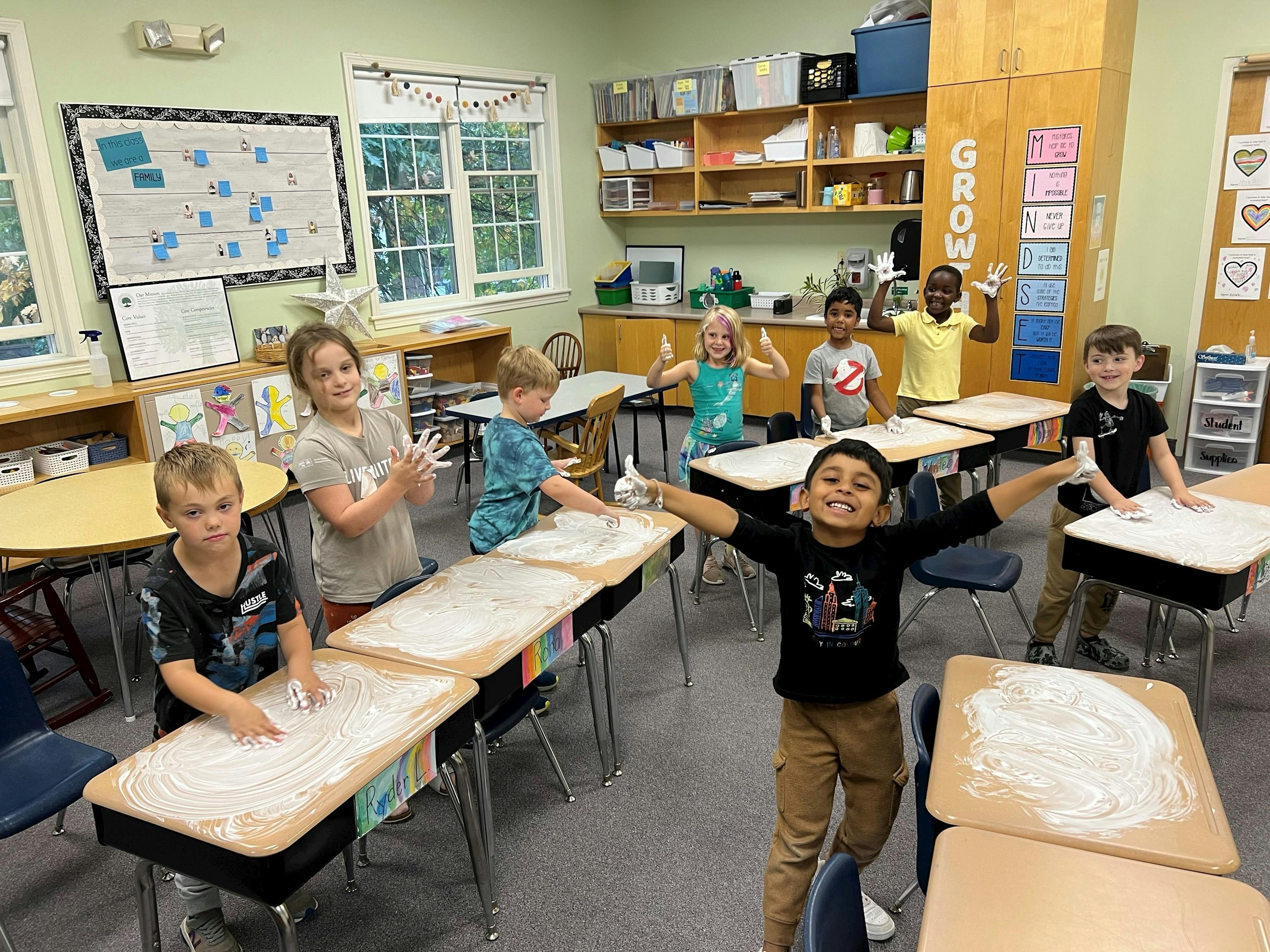 Group of children playing with shaving cream on desks in a classroom