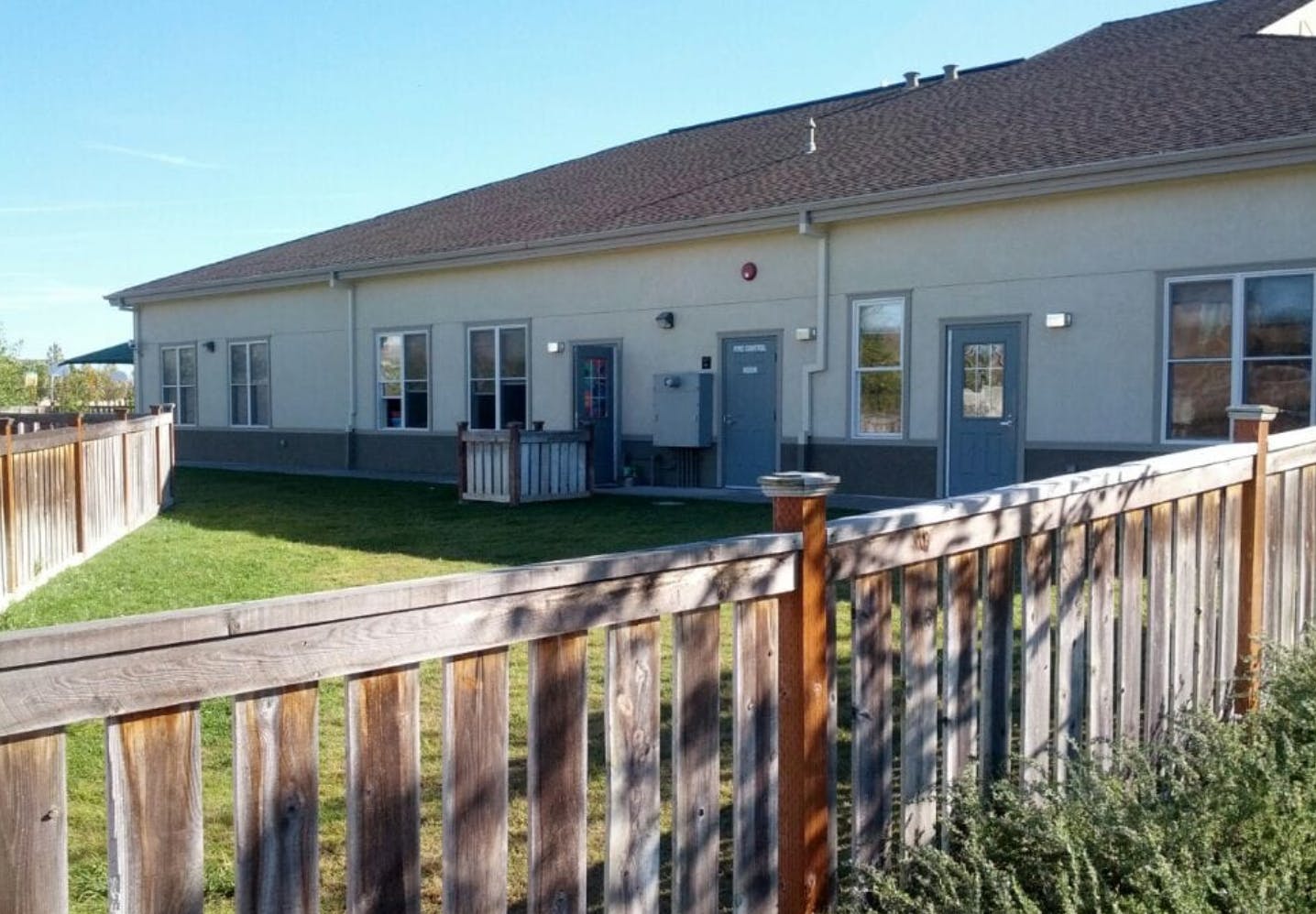Building exterior with multiple doors and windows behind a wooden fence