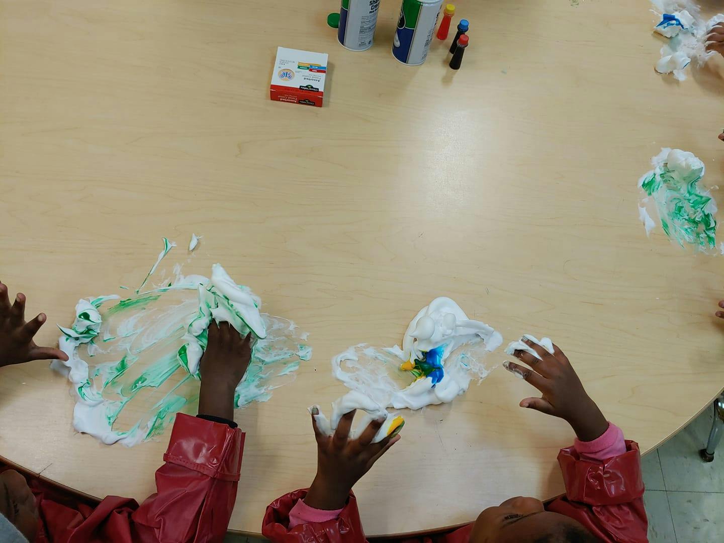 Children's hands playing with shaving cream and paint on a table