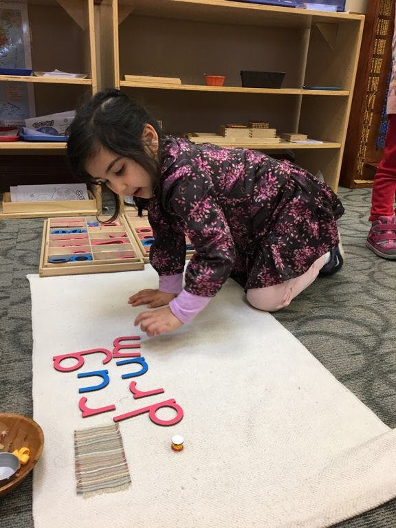Child on floor arranging letter cutouts on a white mat in a classroom