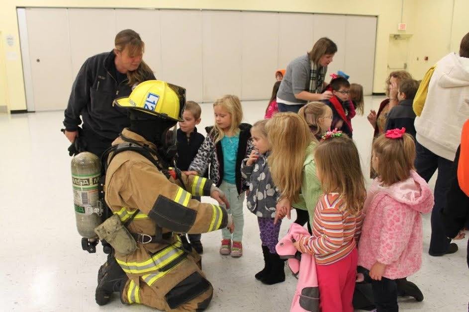 Firefighter in full gear kneeling with children gathered around