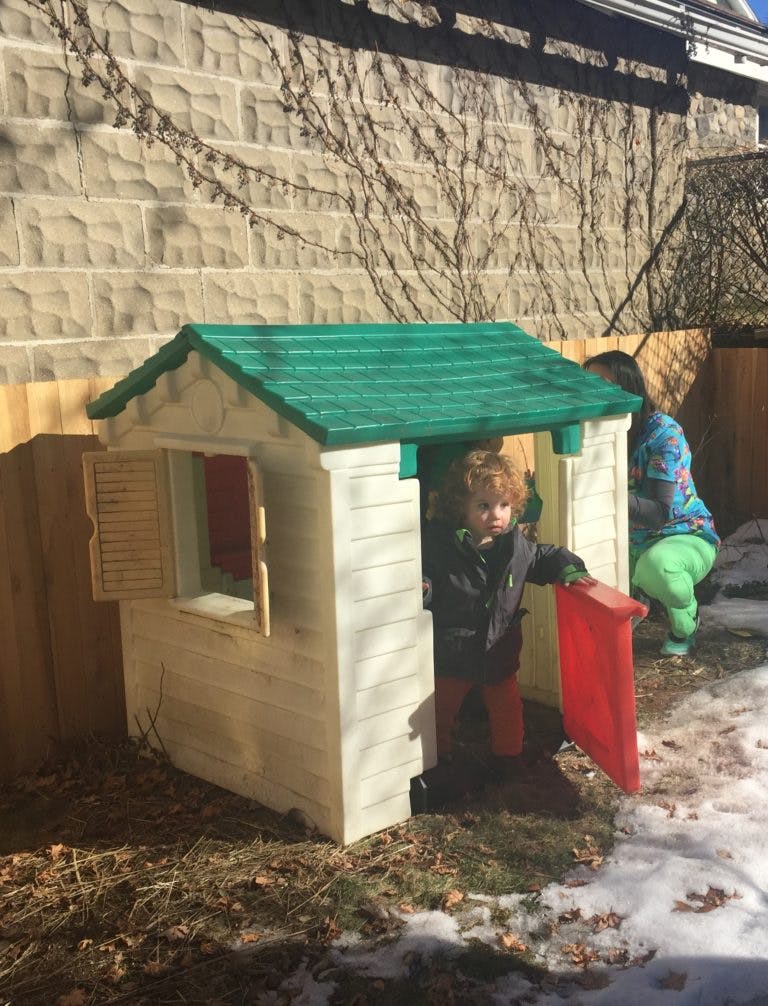 Child standing in a small playhouse with a red door