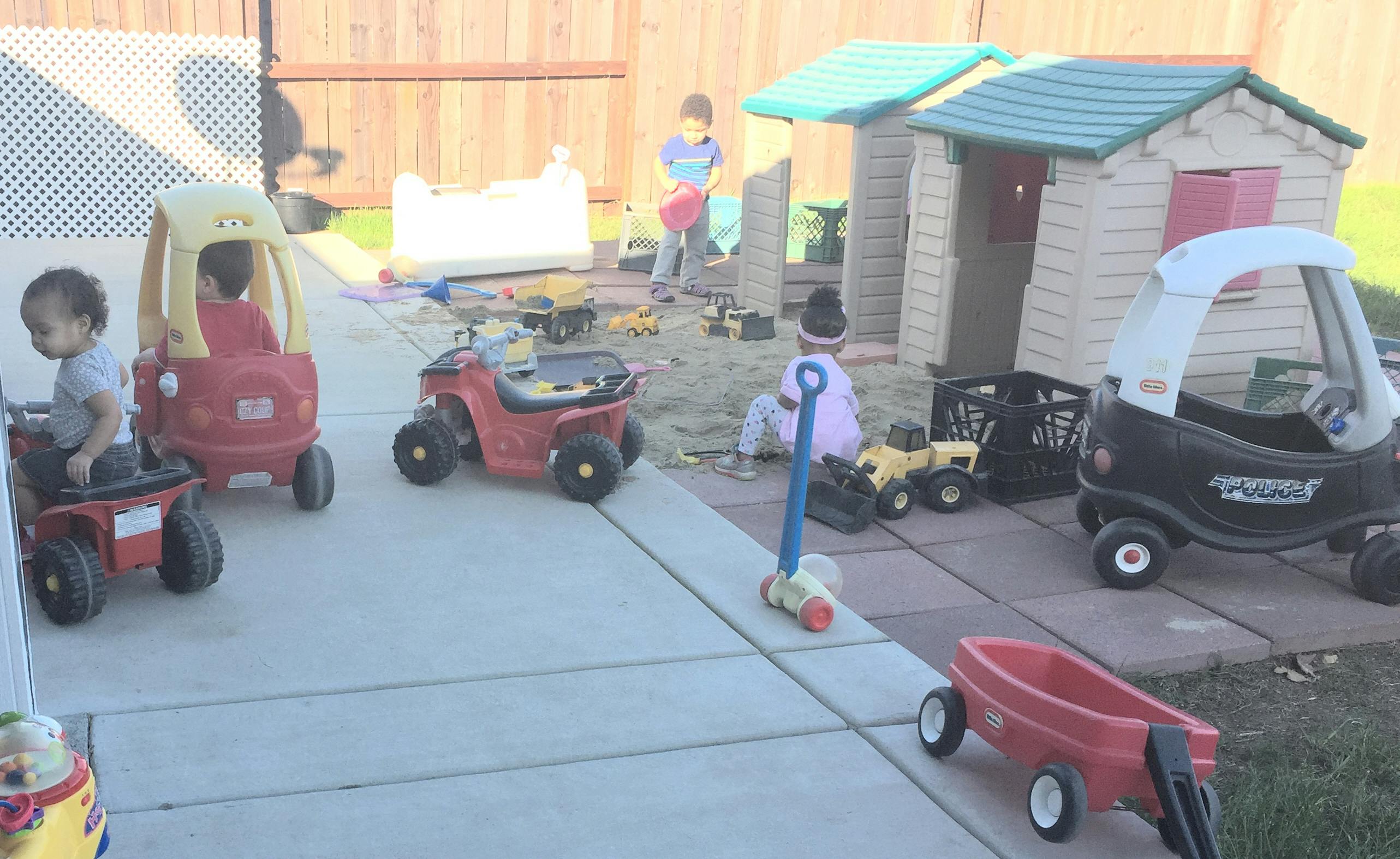 Children playing with toy cars and a playhouse in a yard