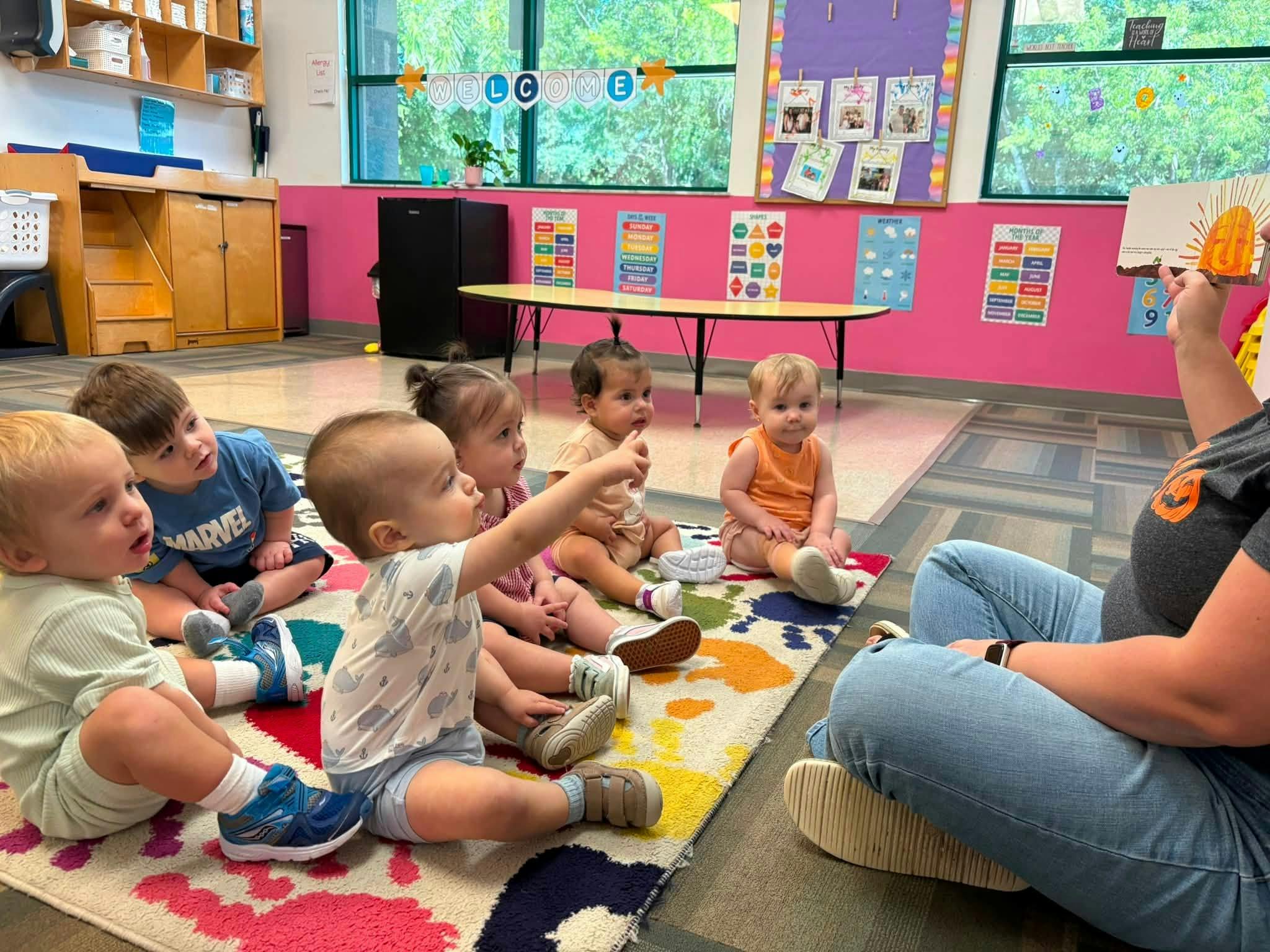 Adult reading a book to a group of young children sitting on a classroom rug