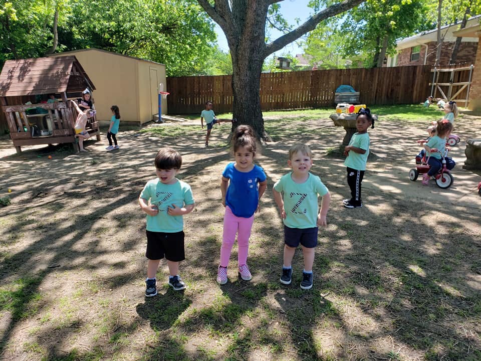 Three children standing in a playground with other children in the background