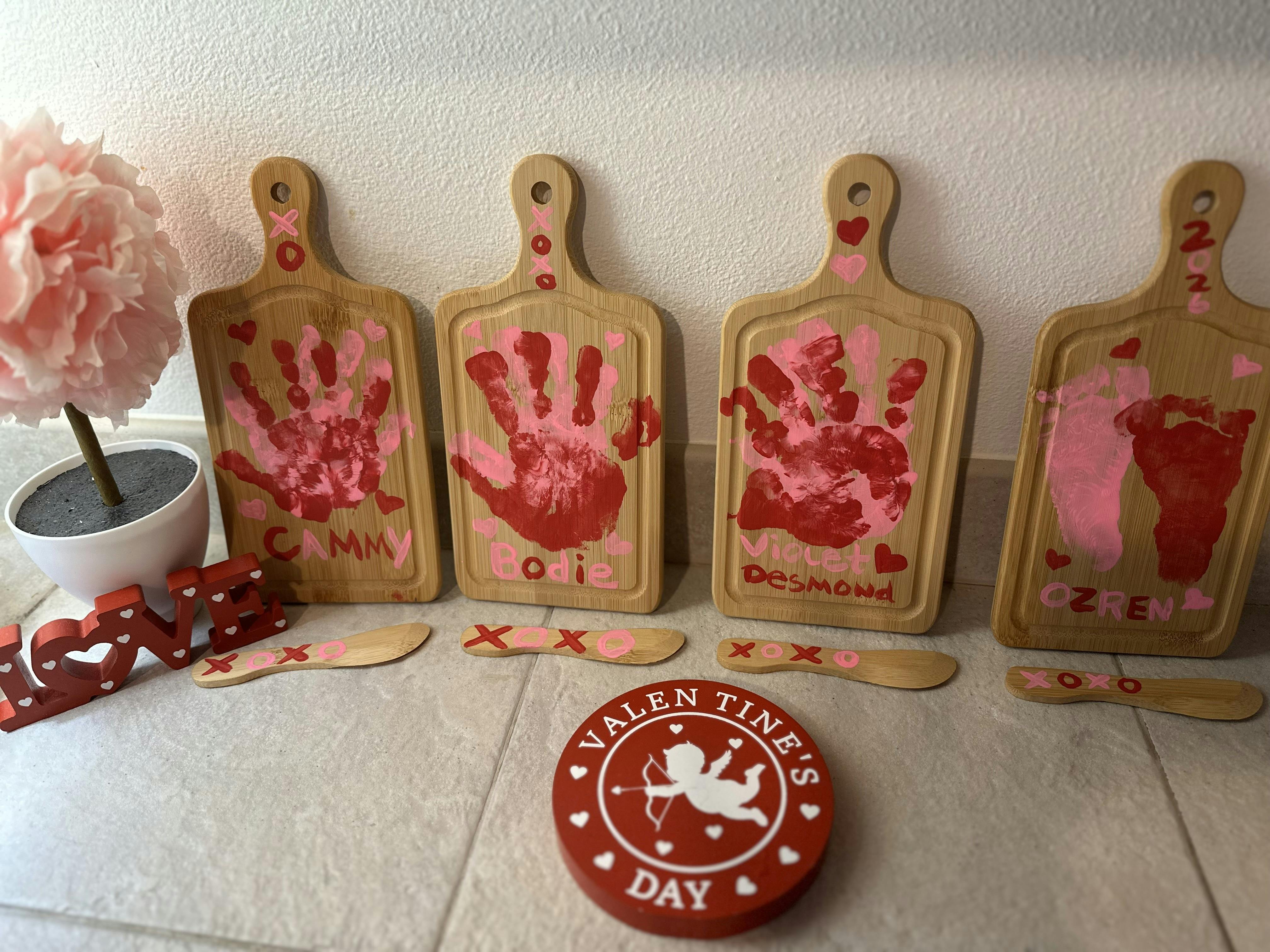 Four wooden cutting boards with pink and red handprints and footprints