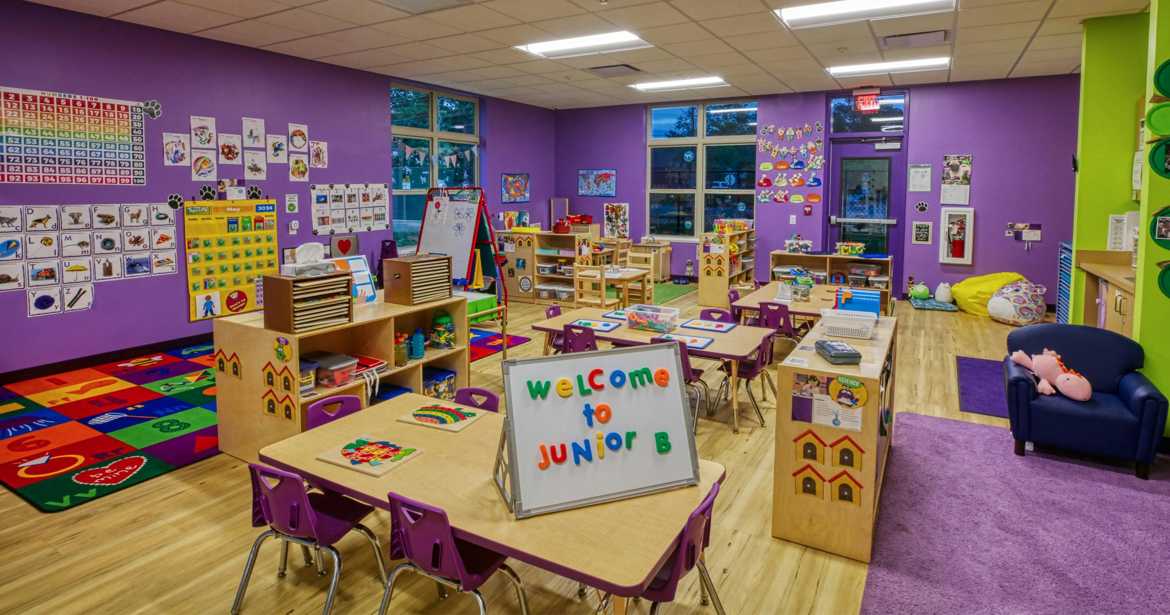 Classroom with purple walls, tables, and a whiteboard reading "WELCOME to Junior B"