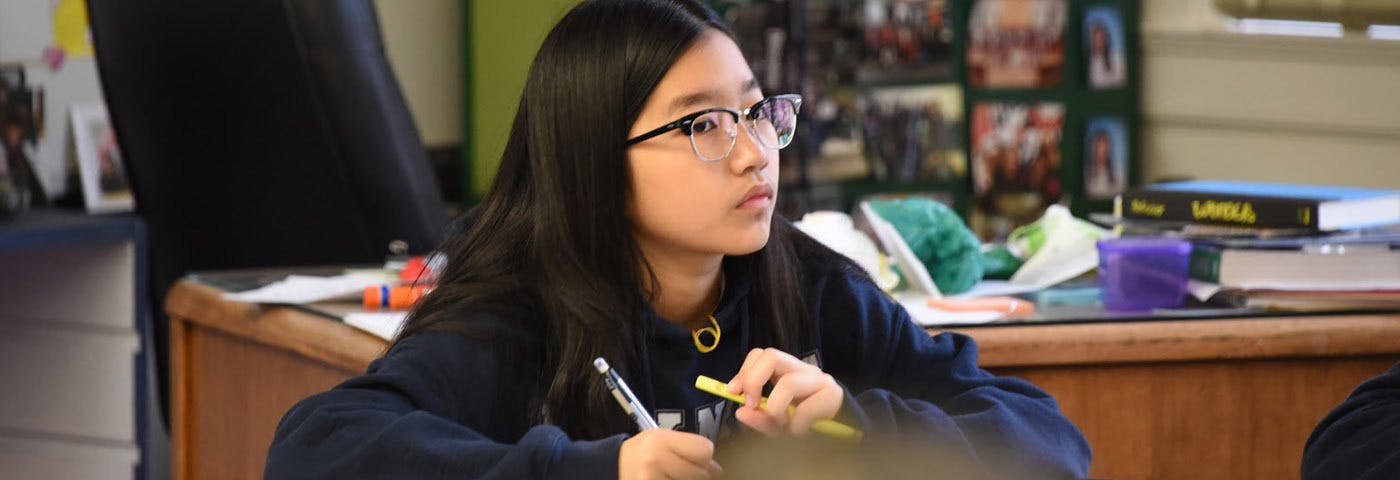 Teenager in glasses holding a pencil in a classroom