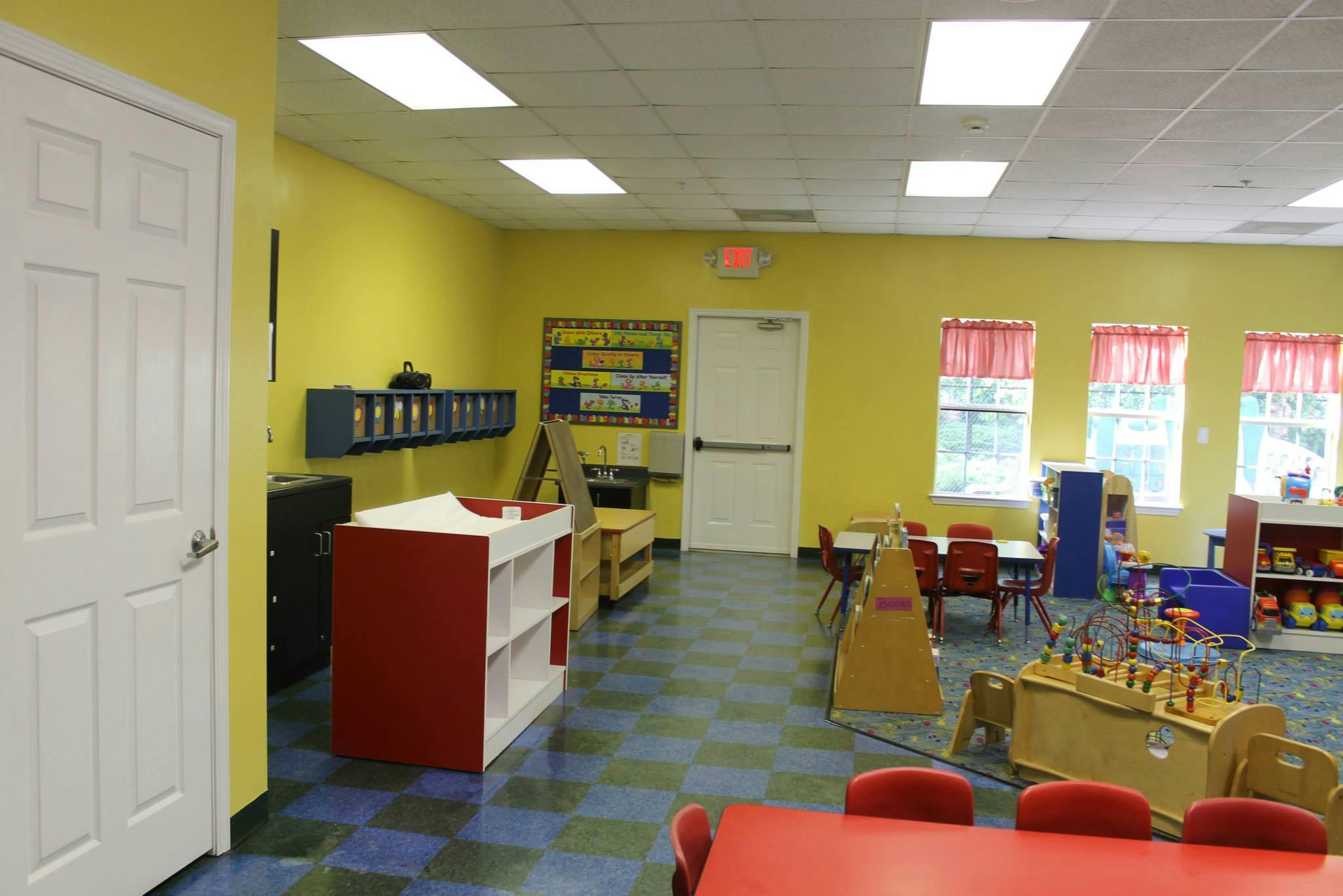 Classroom with yellow walls, blue and green checkered floor, small tables and toys