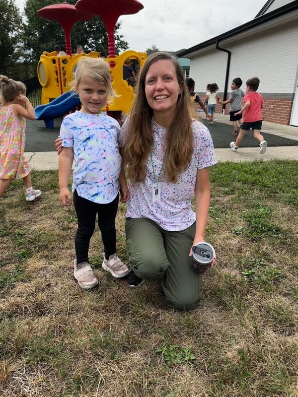 Adult and child posing on grass with playground in background