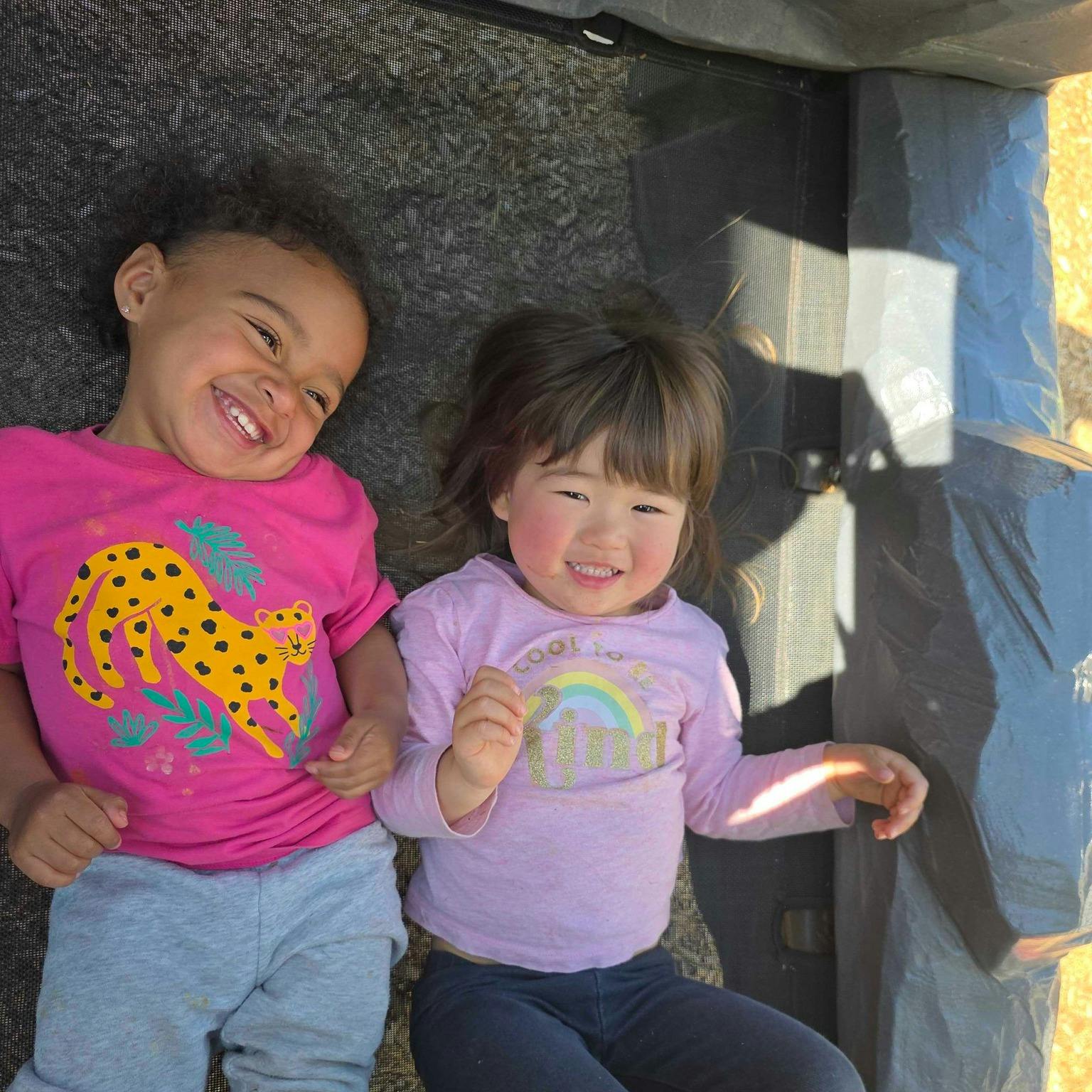 Two smiling children lying down together outdoors