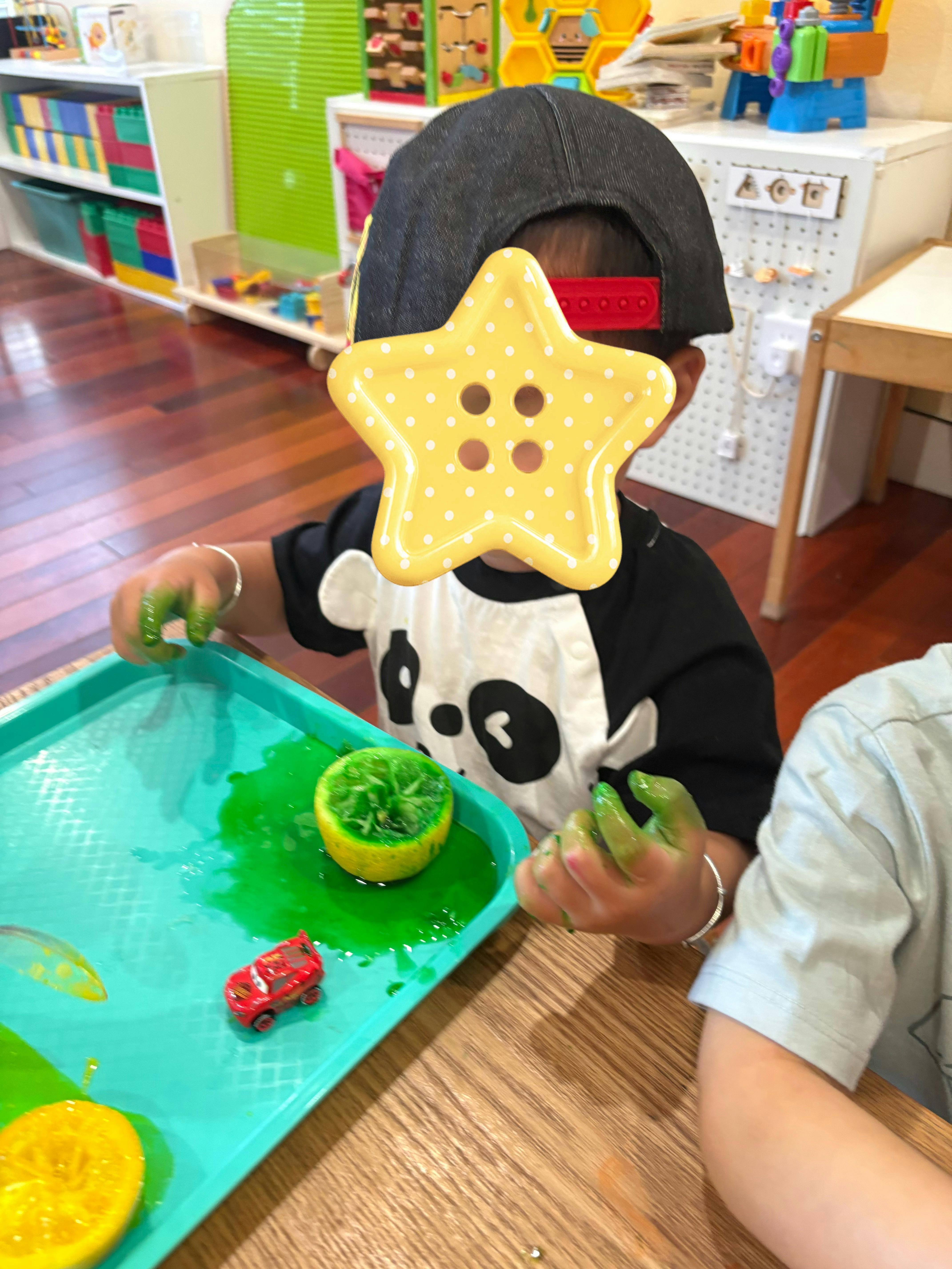Child with green paint on hands playing with halved citrus fruit on a tray