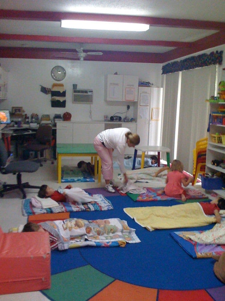 Person bending over children sleeping on mats in a room