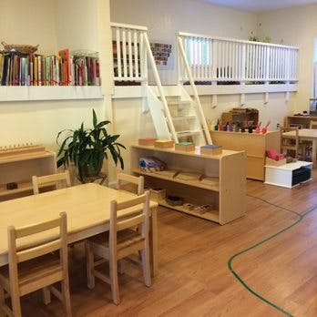 Classroom with tables, chairs, shelves, and a loft area with a railing and railing