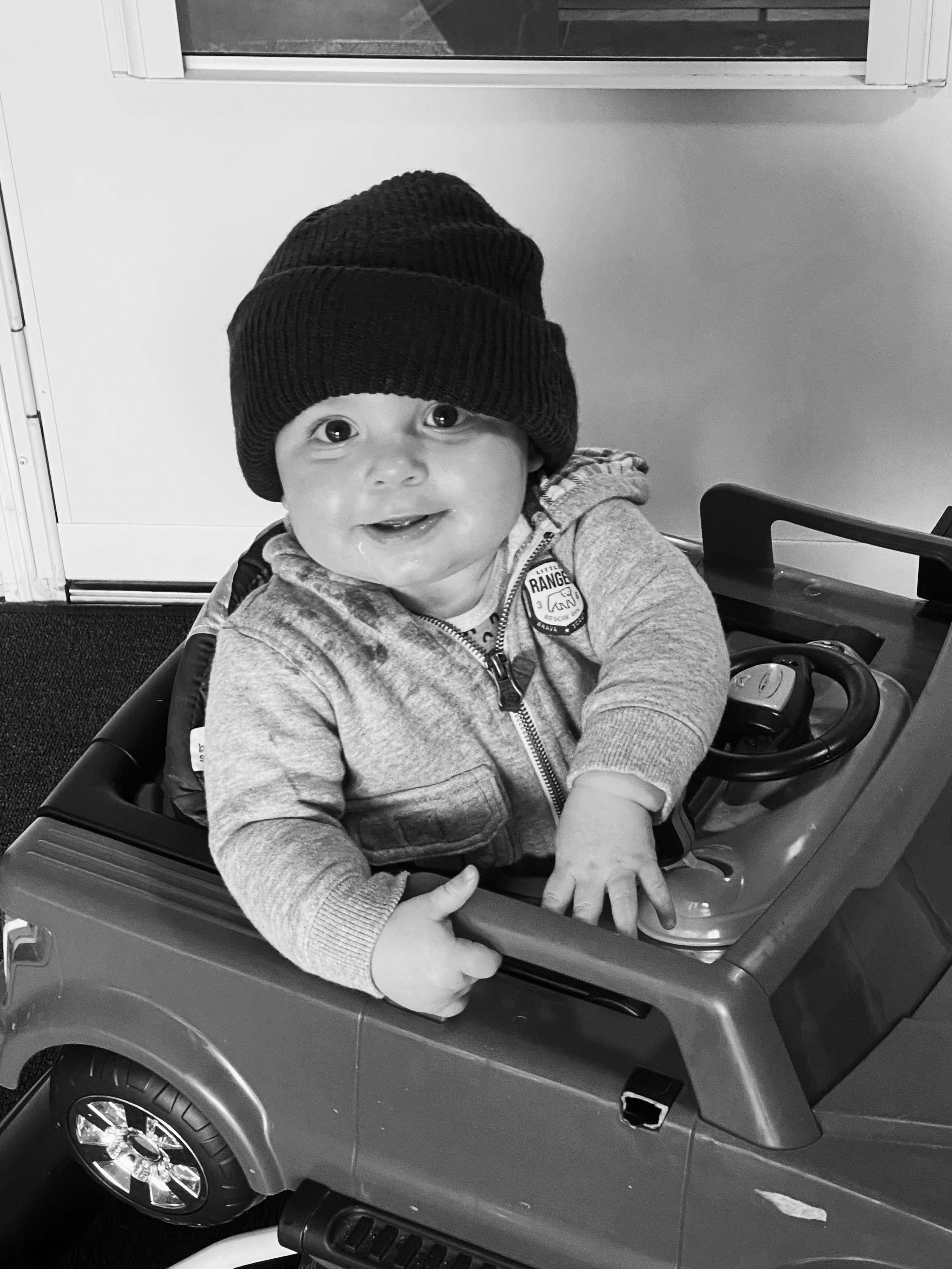Child wearing a knit hat sitting in a toy car