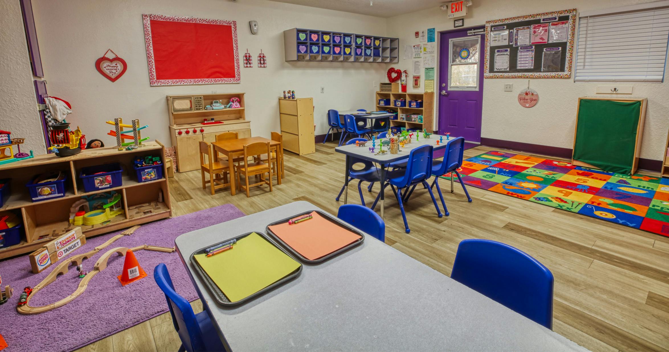 An empty colorful classroom with small tables and chairs and various play areas