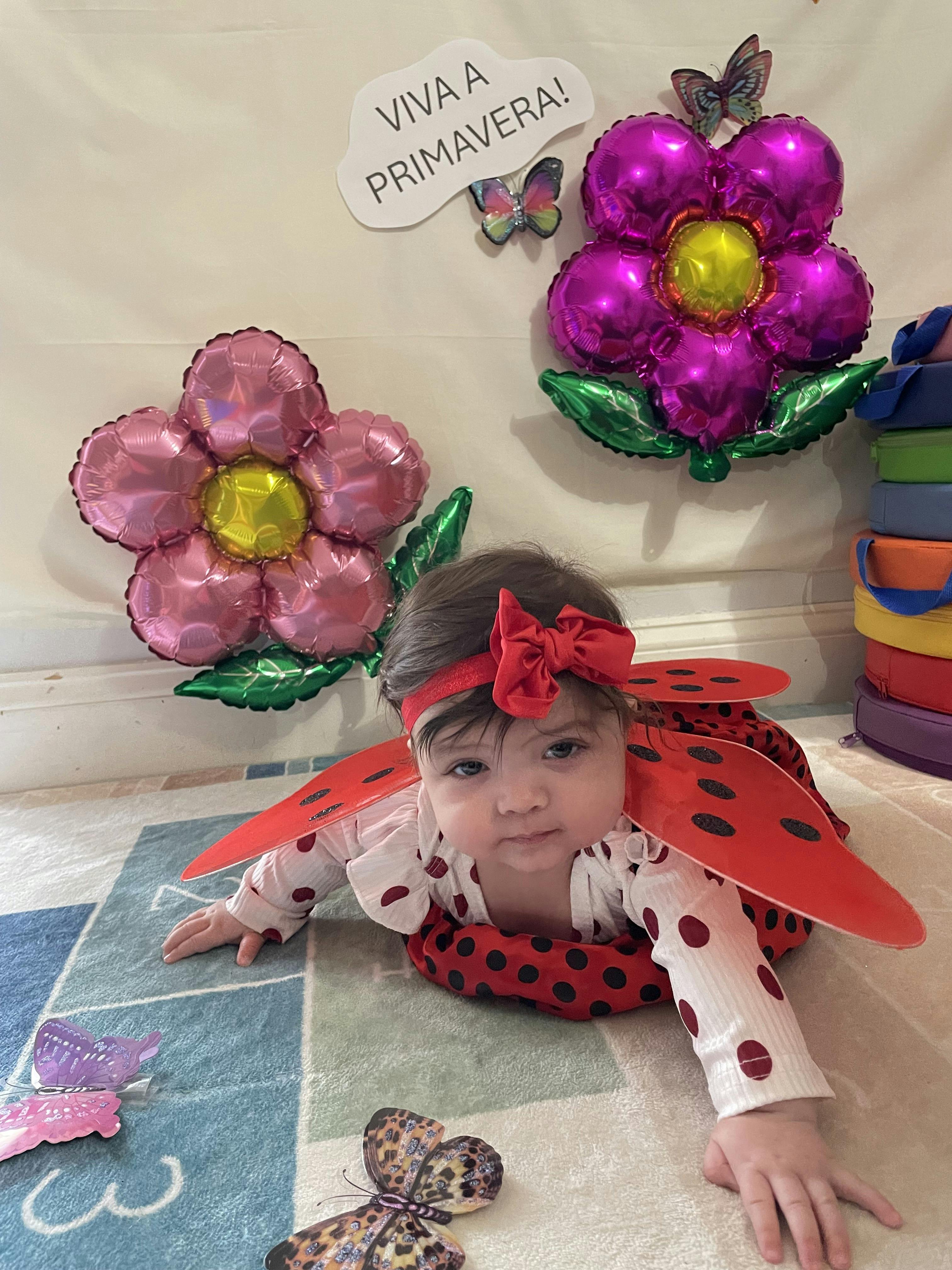 Child in a ladybug costume crawling on a rug with flower balloons