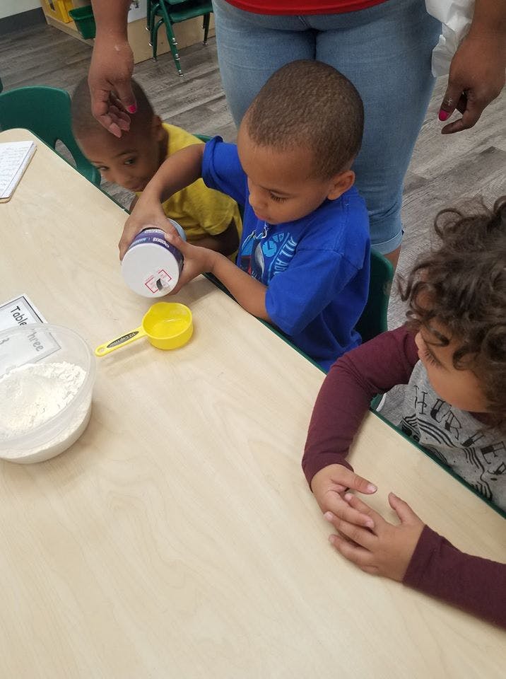 Child pouring from a container into a measuring cup at a table