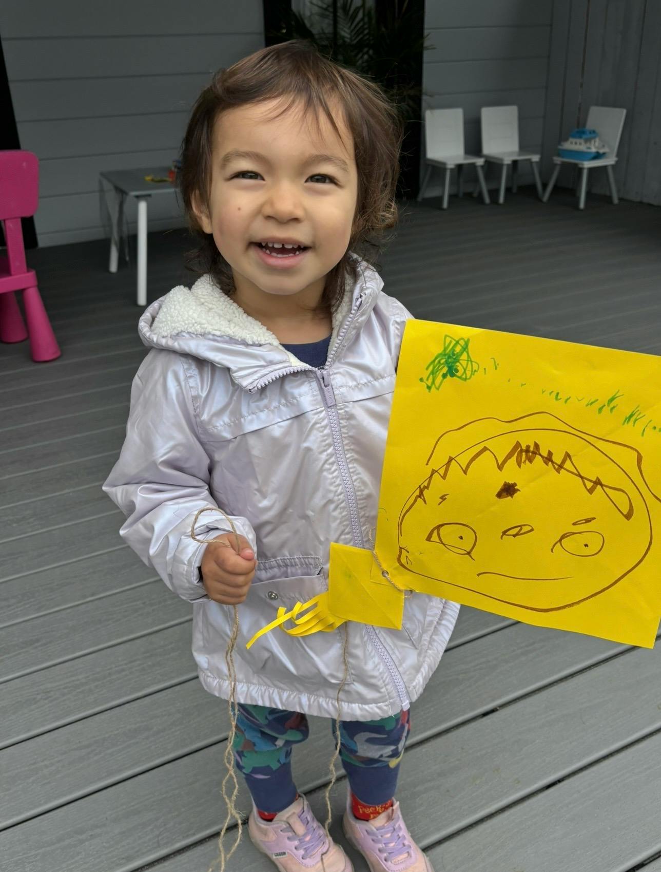 Child holding a yellow paper drawing of a face