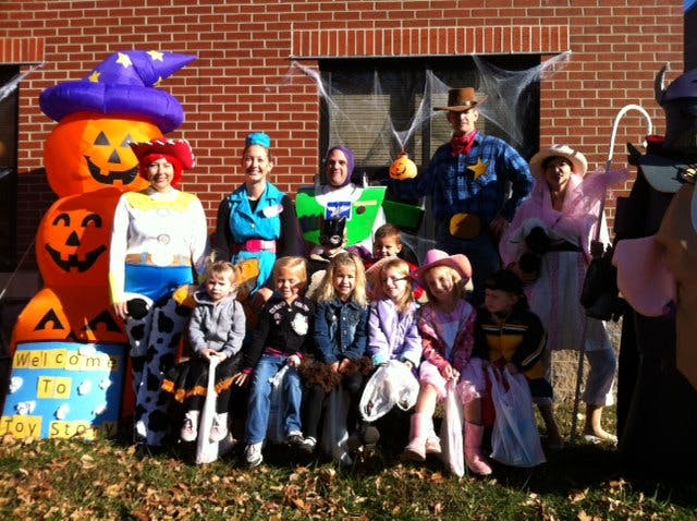 Adults and children in Halloween costumes posing in front of a brick building