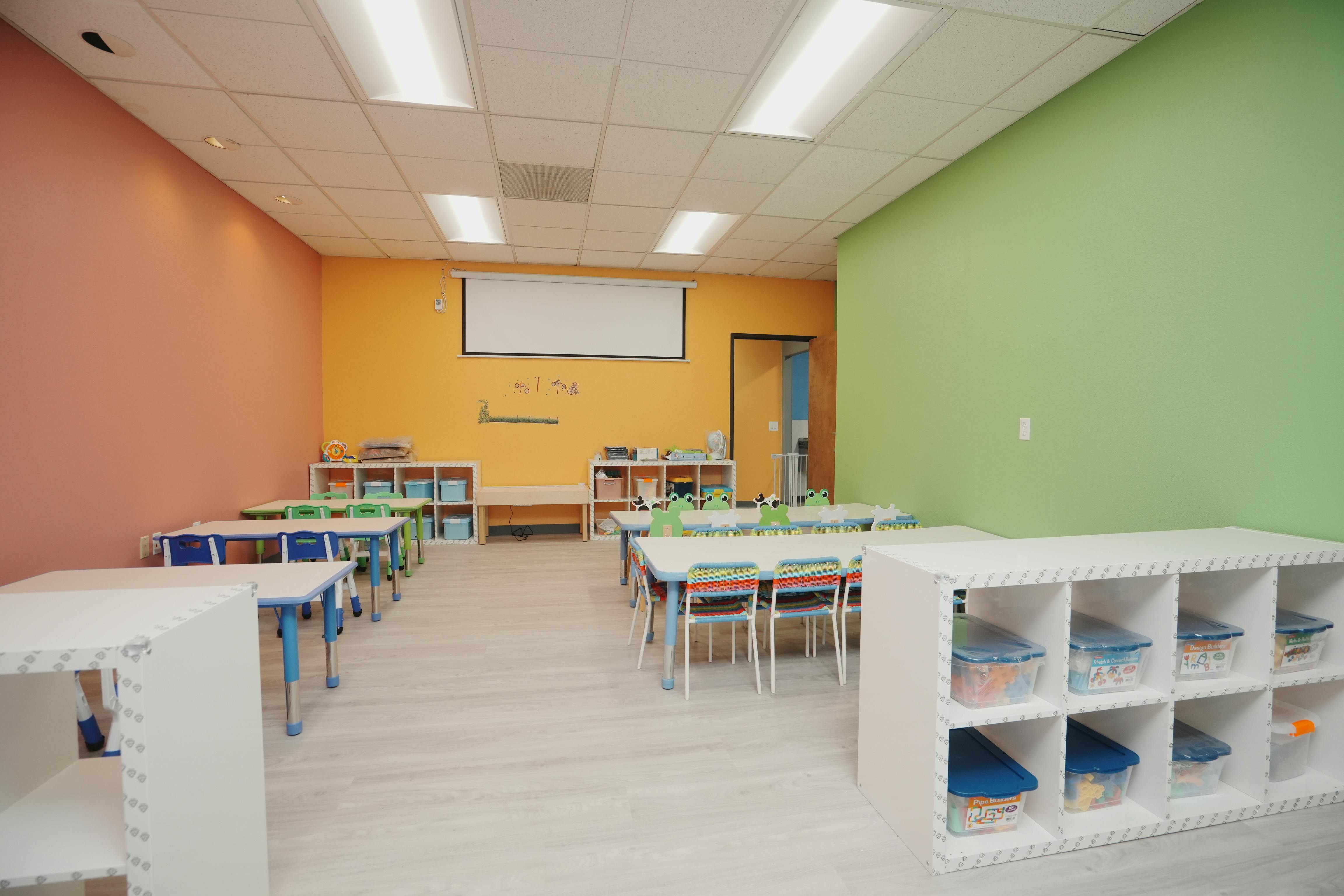Empty classroom with colorful walls, tables, chairs, and storage shelves