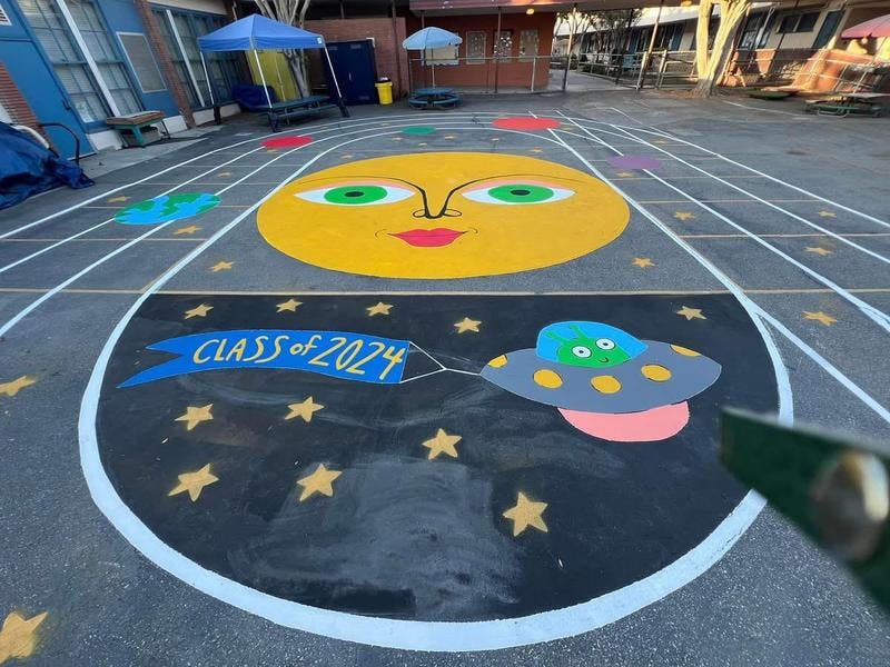 Solar system mural with a sun and a UFO pulling a banner that says “Class of 2024”