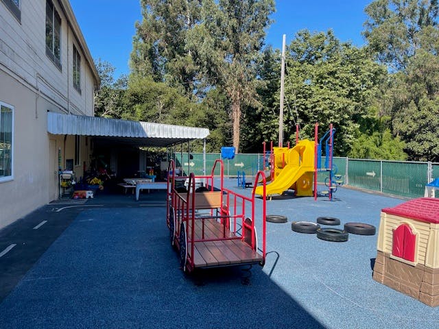 Outdoor playground with yellow slide, red wagon, and small playhouse
