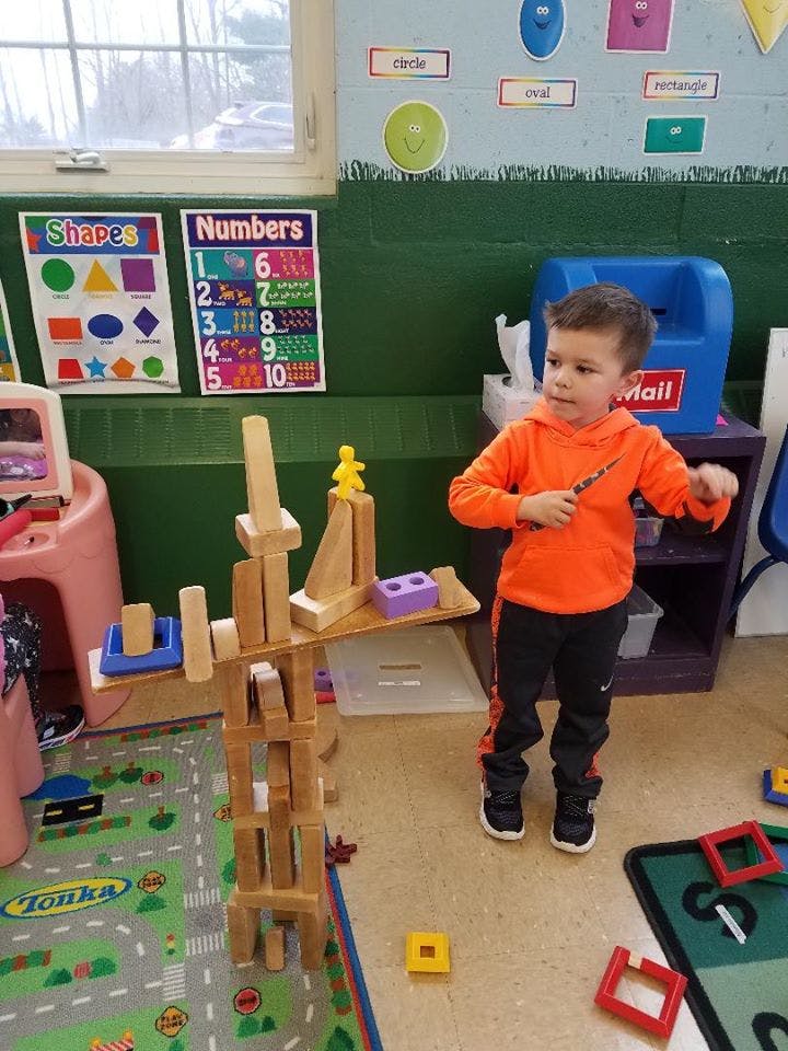 Child standing next to a tall structure made of wooden blocks