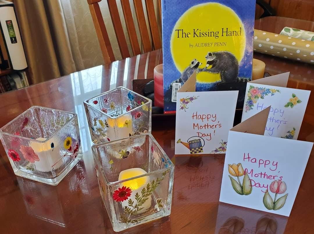 Four glass candle holders with candles, Mother's Day cards, and a book