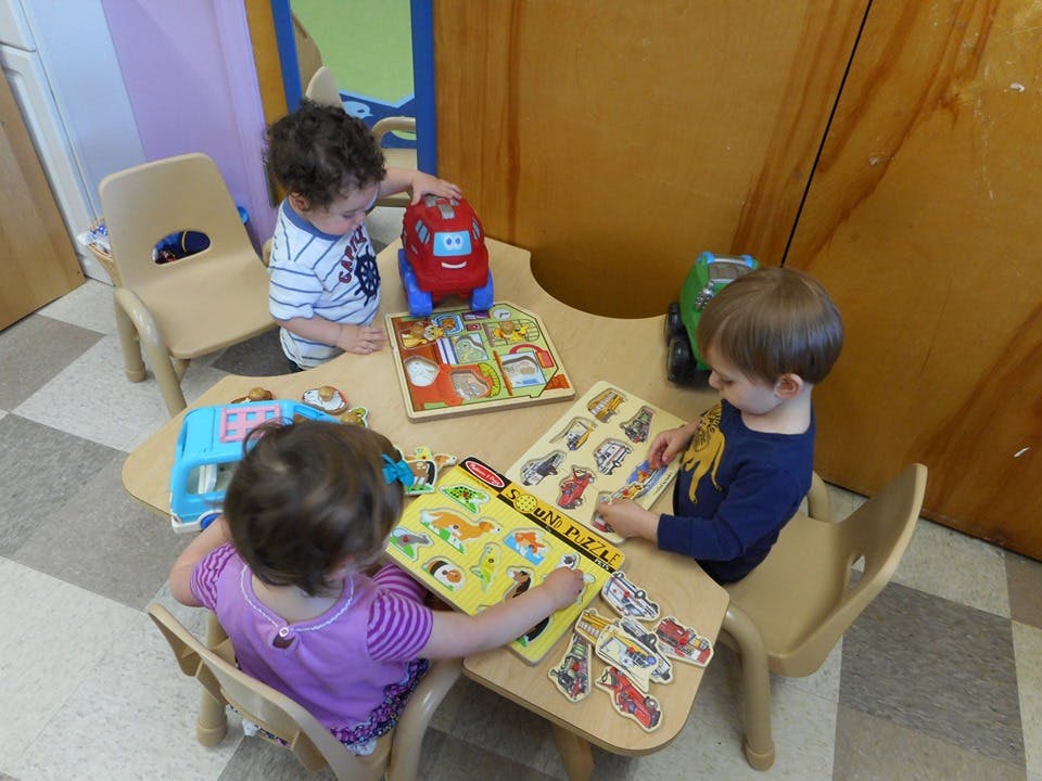 Three children playing with puzzles and toys at a small table
