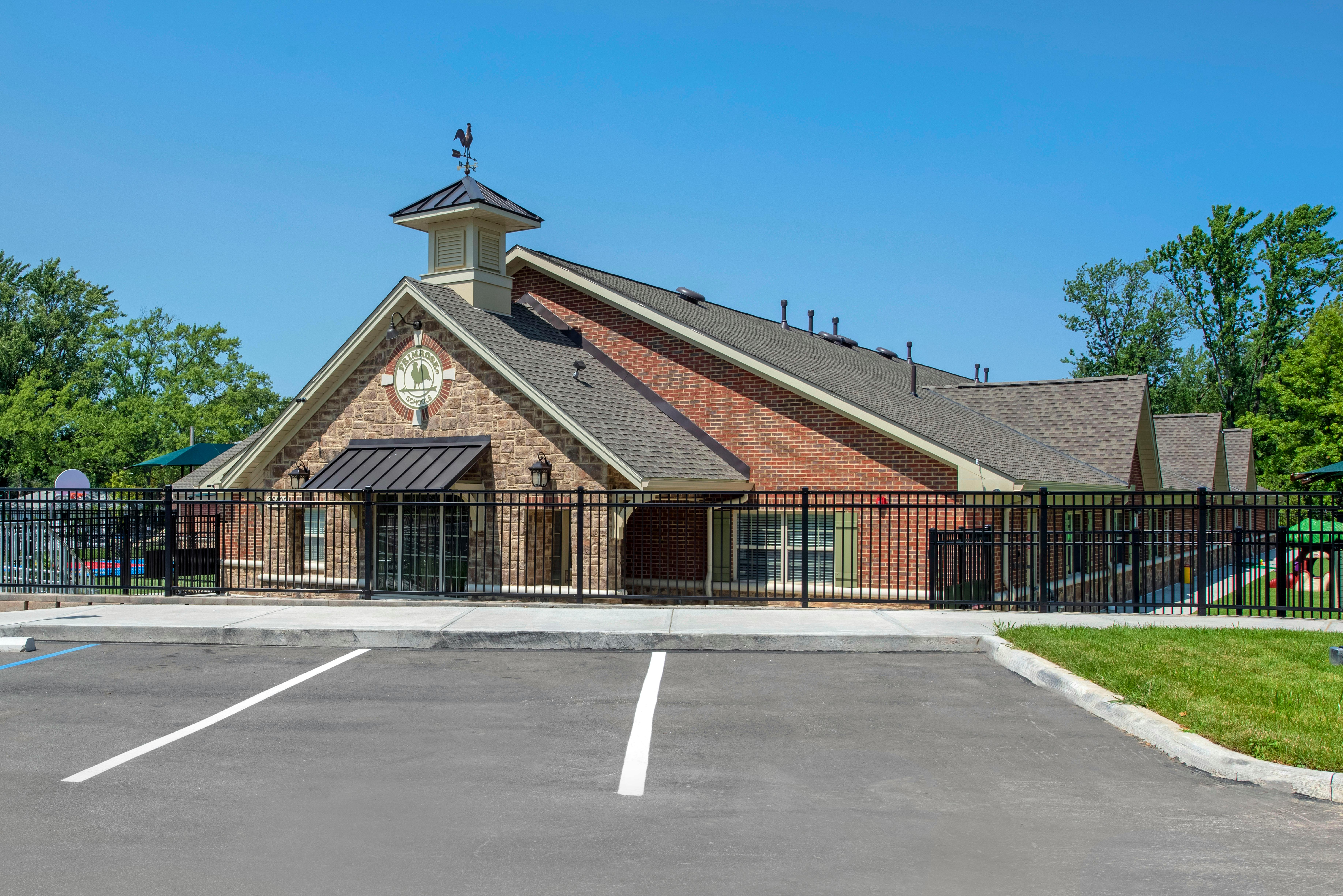 A Primrose School building with stone and brick exterior, a weathervane, and a parking lot