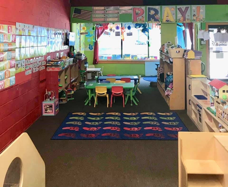 Classroom with small tables and chairs, shelves, and a rug with car designs