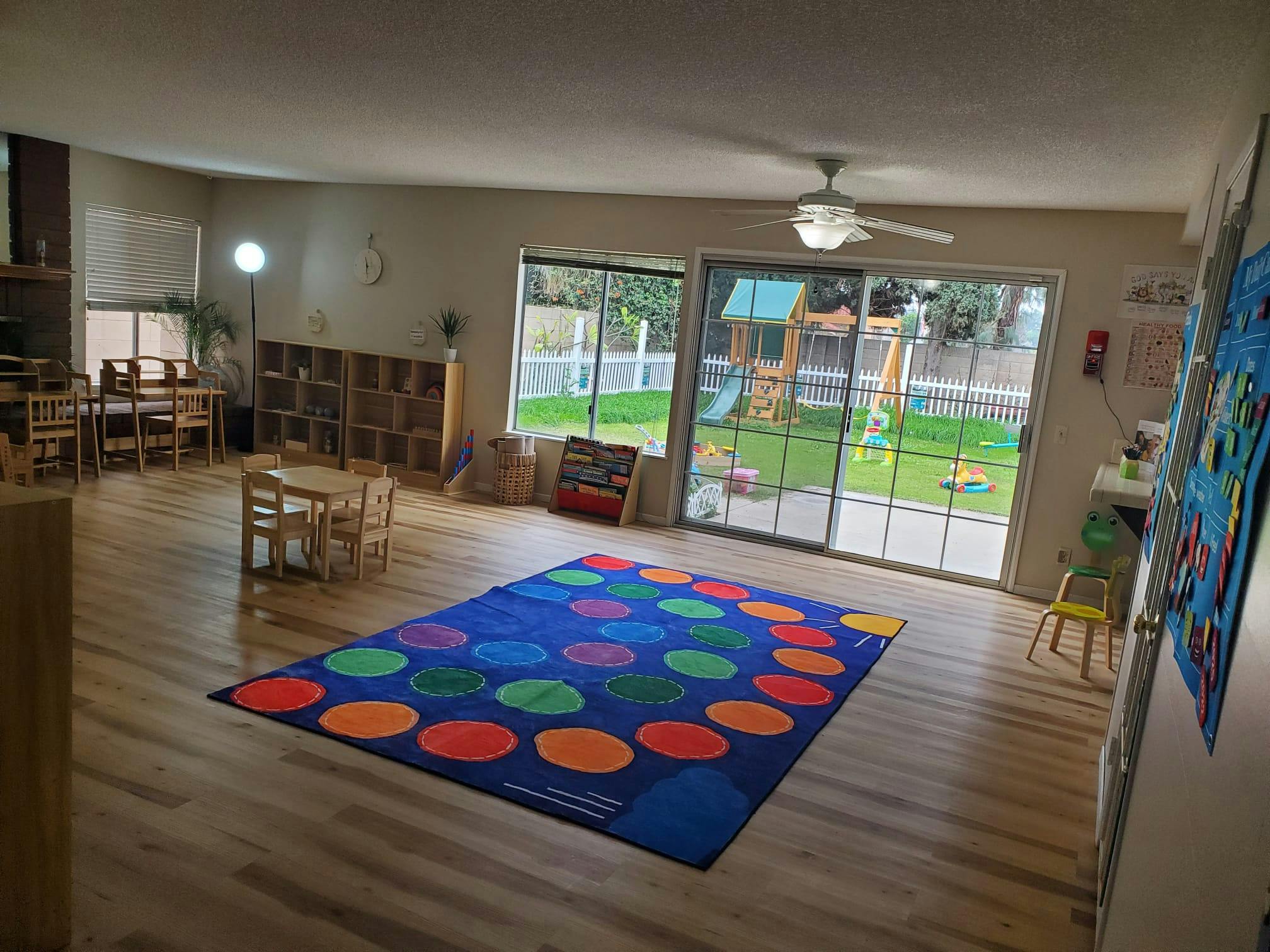 Classroom with a colorful rug, small tables and chairs, and a view of a playground