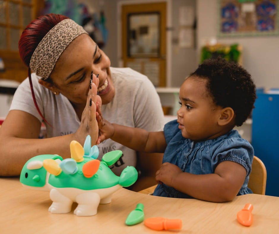 Adult and child playing with a dinosaur toy in a classroom