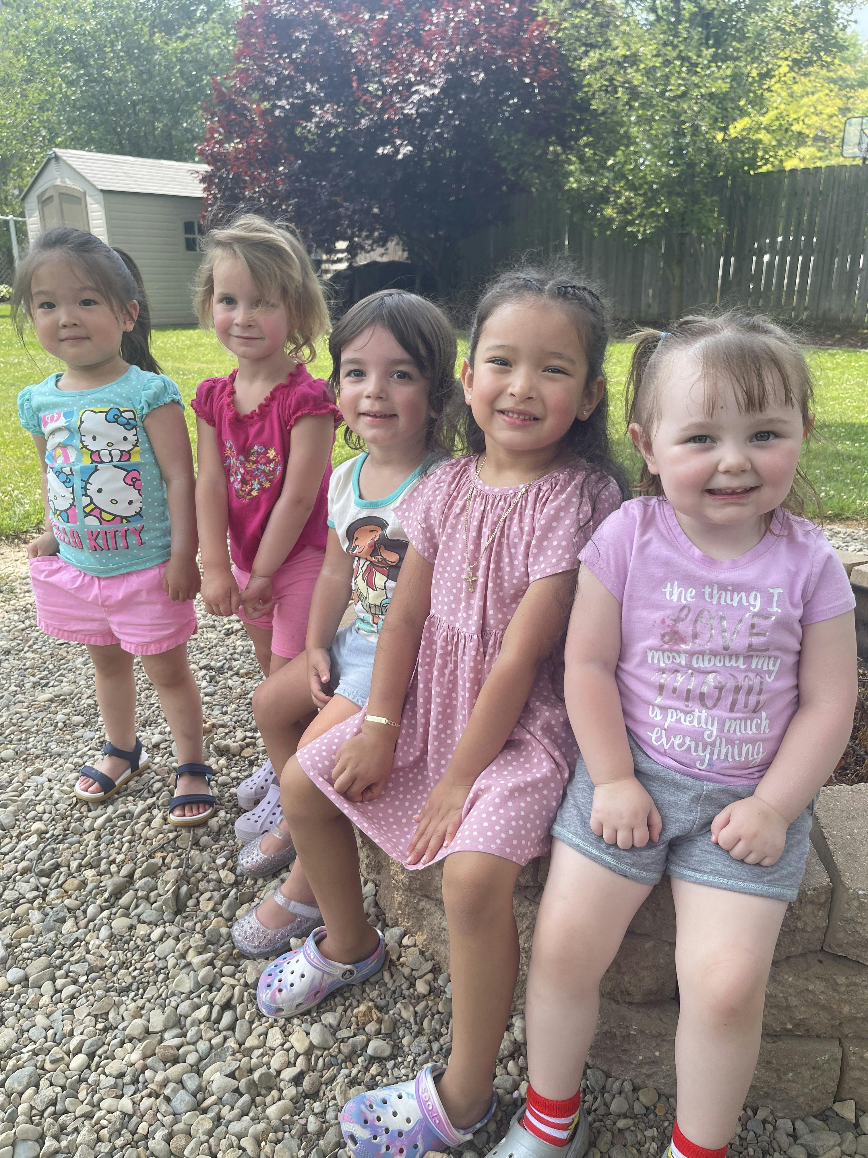 Five children posing together outdoors on a gravel surface