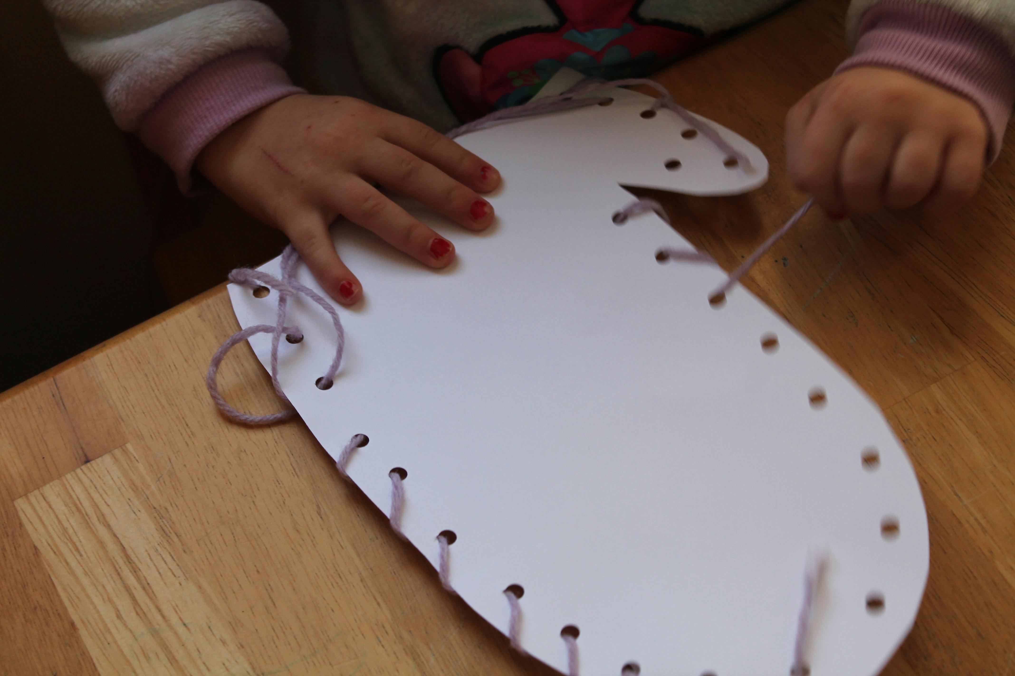 Child lacing string through holes in a paper shape