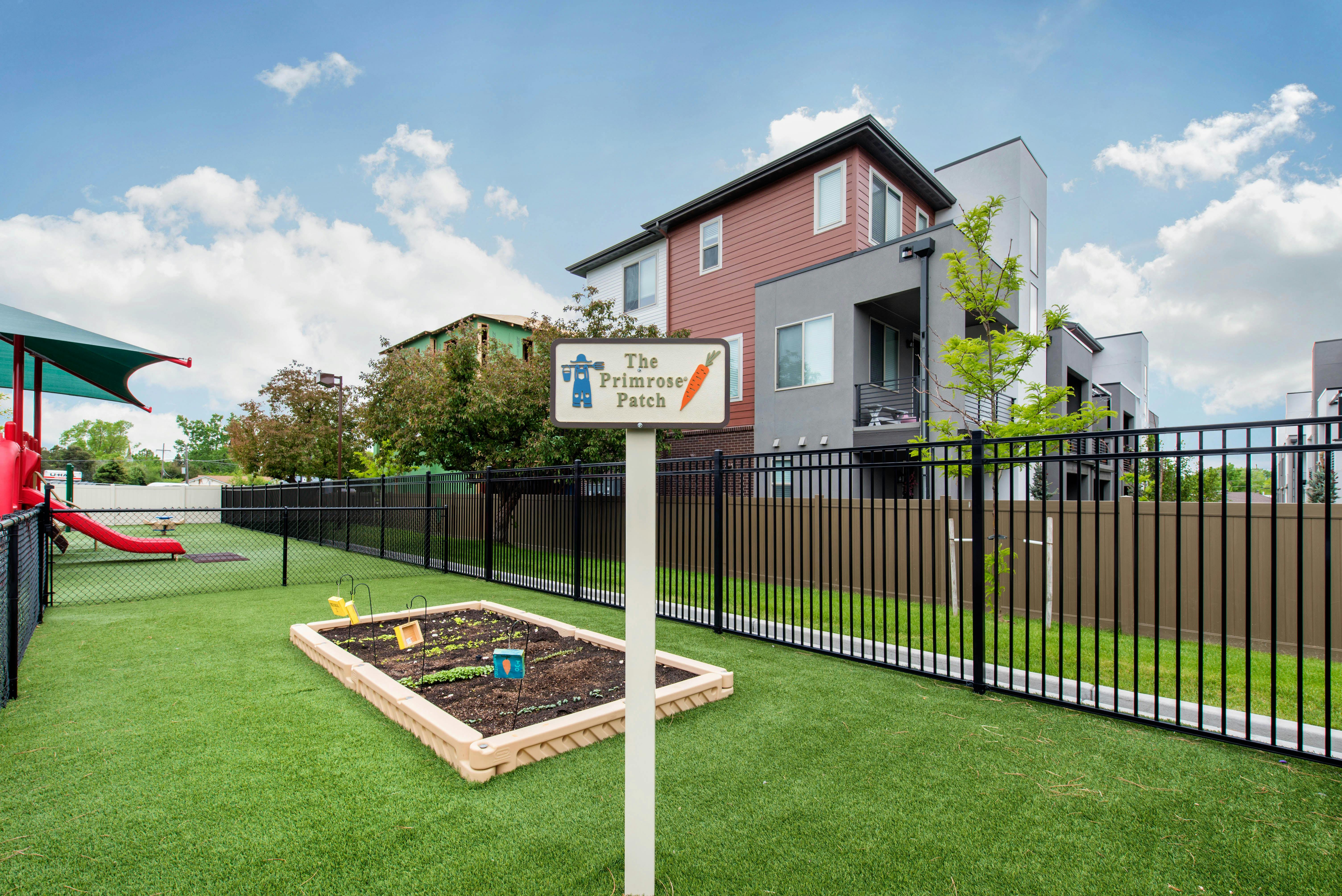 A fenced playground area with artificial turf and a raised garden bed labeled The Primrose Patch