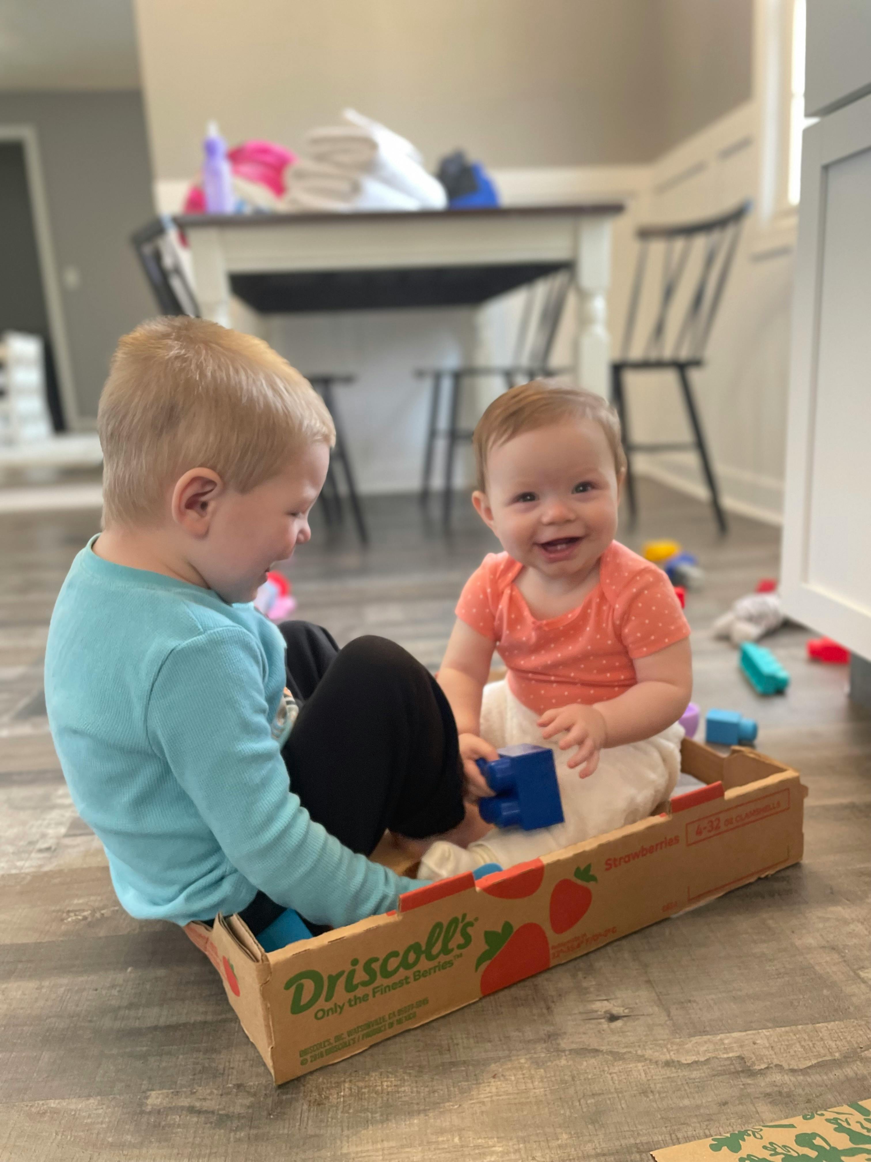 Child and baby playing in a cardboard box
